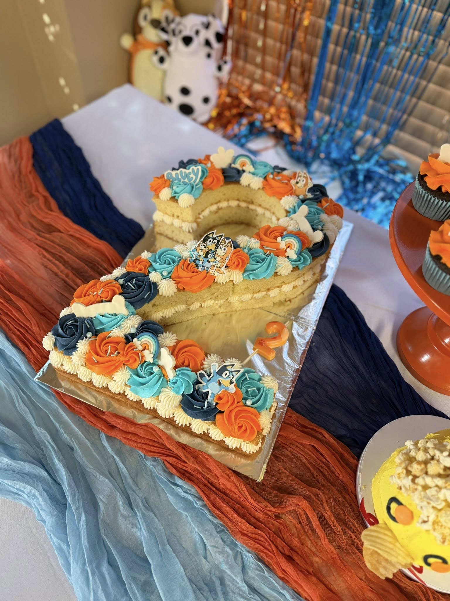 Bluey-themed number two shaped birthday cake decorated with orange and blue frosting swirls.