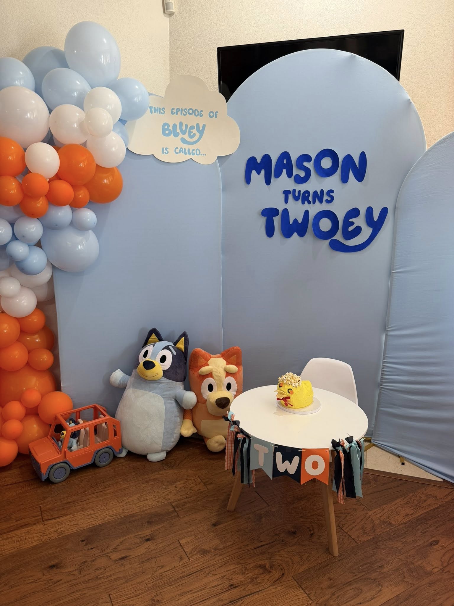 Bluey-themed second birthday party setup featuring Mason's birthday cake on a table and Bluey plush toys.
