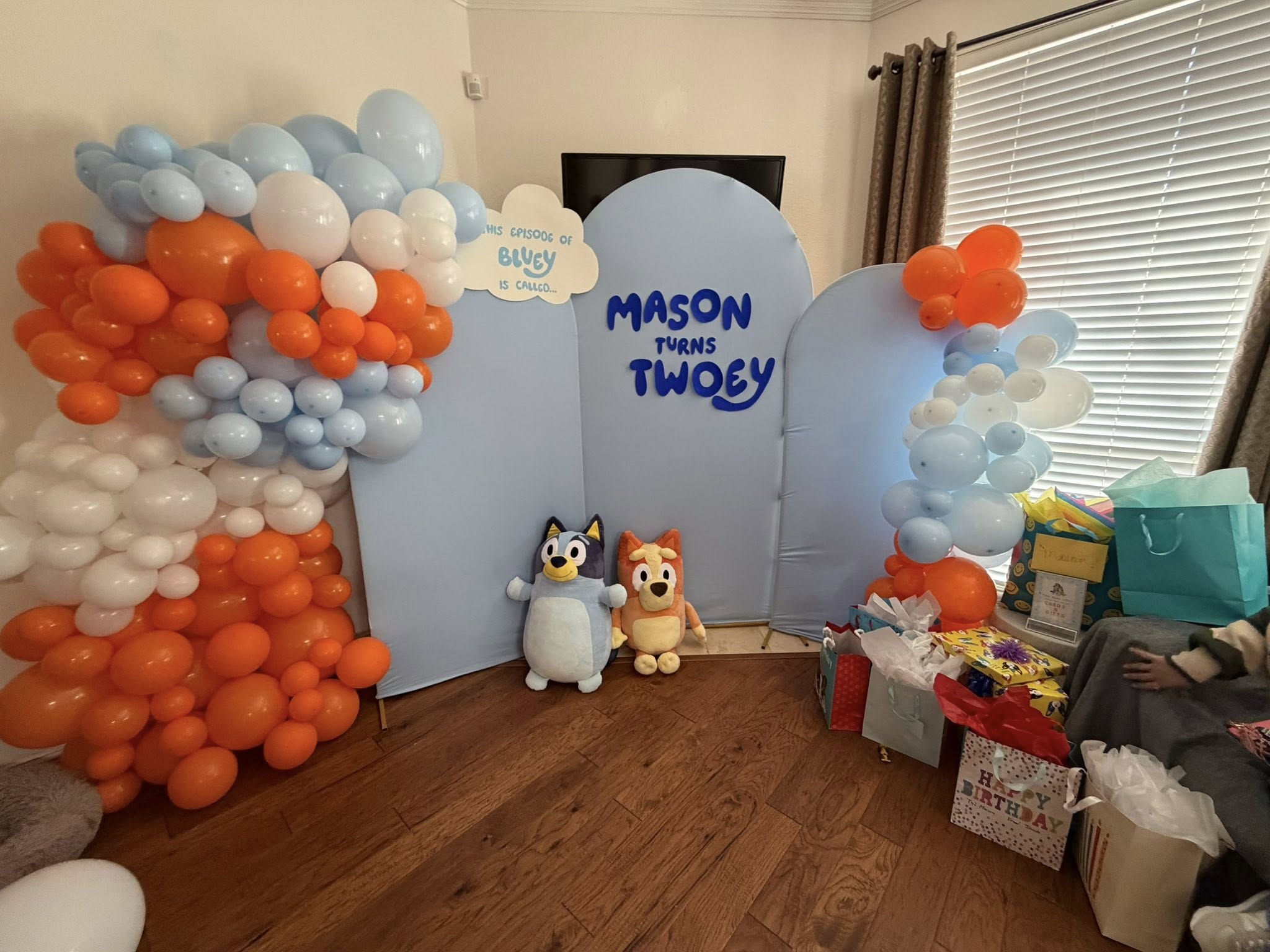 Bluey themed second birthday party backdrop with orange and blue balloons and plush characters.