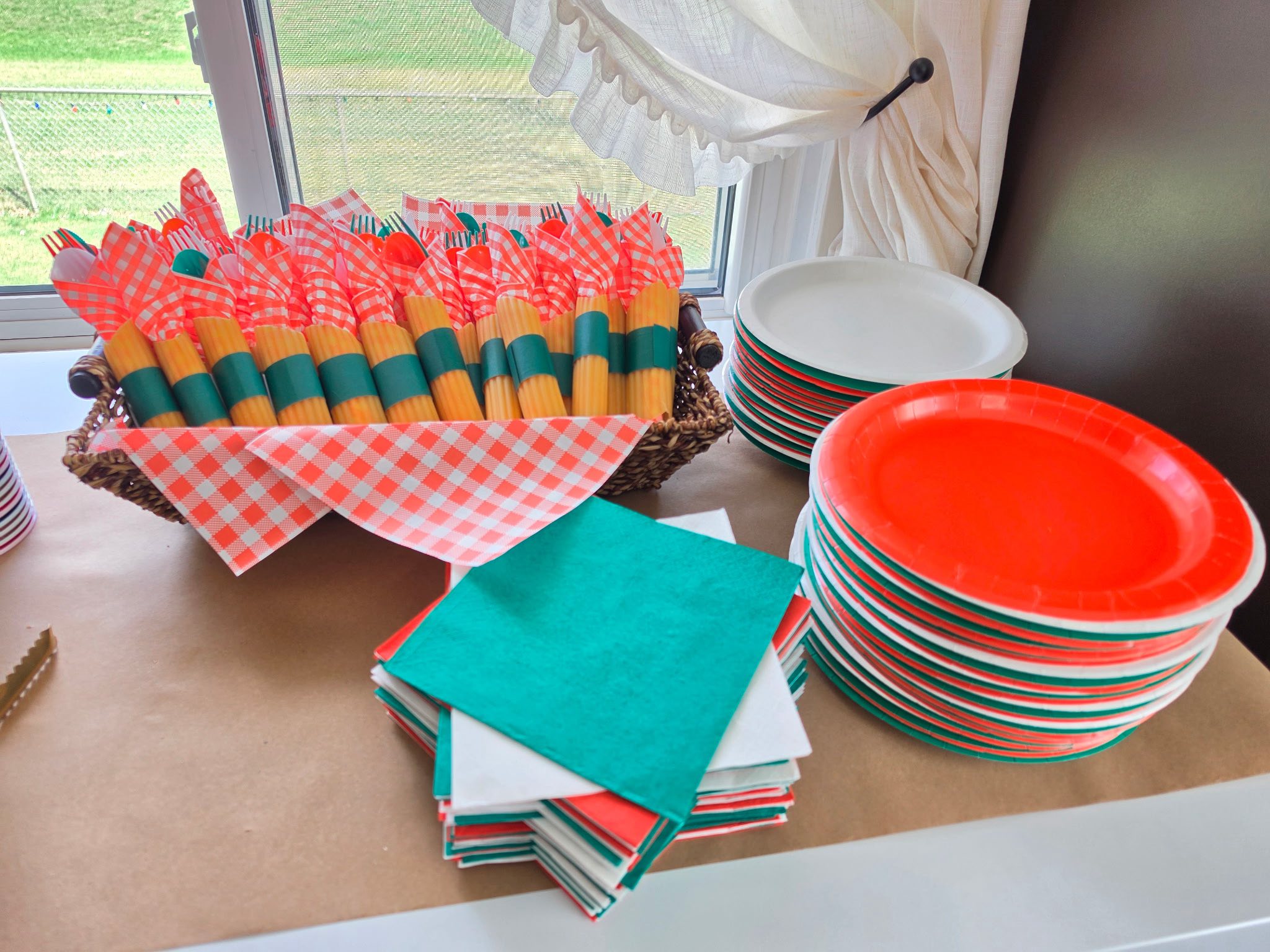 Table setting with red and white checkered napkins, wrapped cutlery, and stacks of red, green, and white plates.