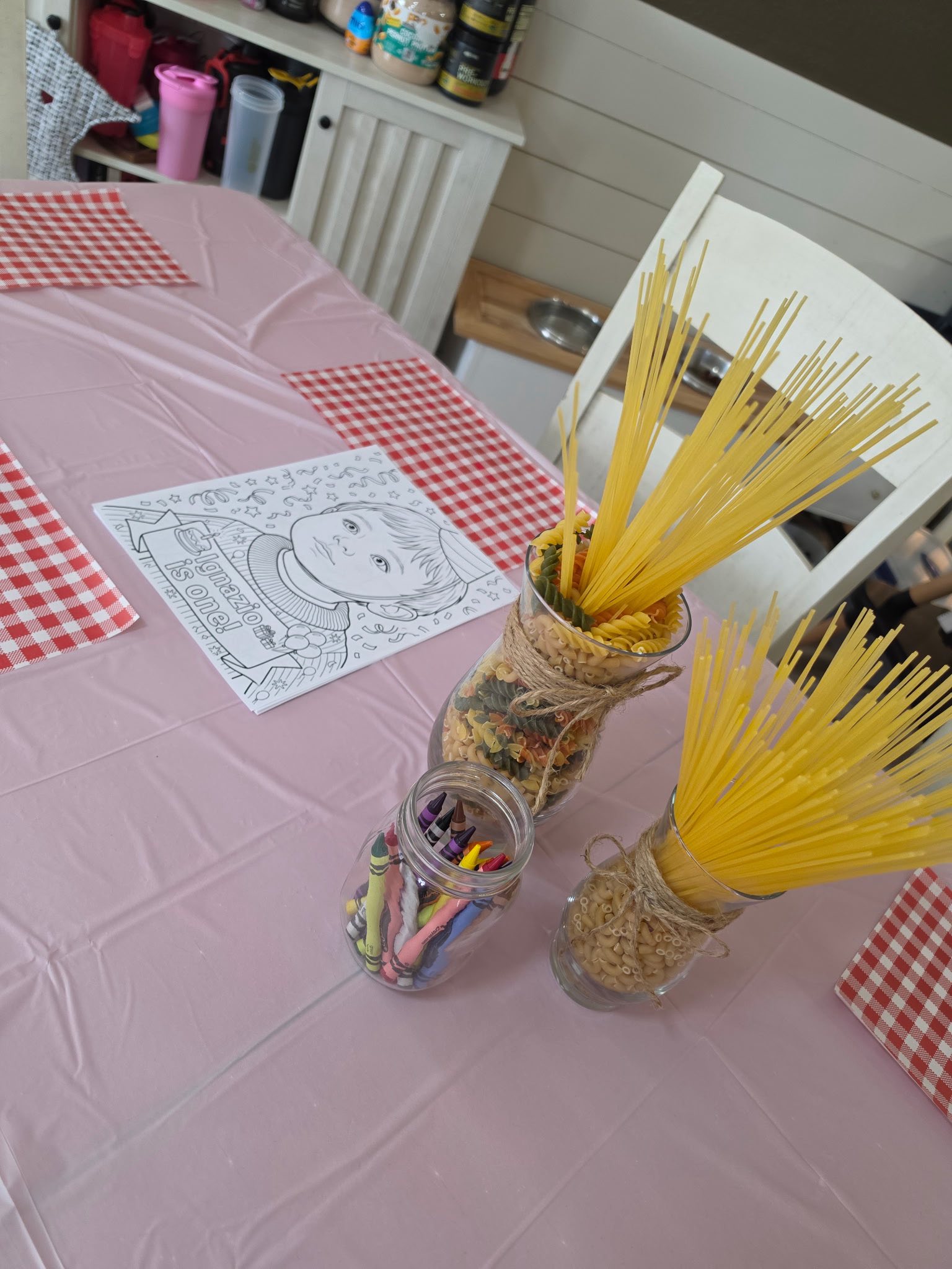 Dining table set for a first birthday party with pasta-themed decorations and macaroni craft activities.