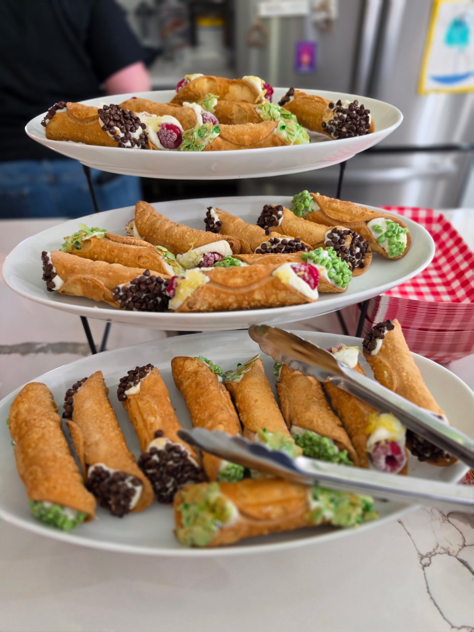 Three-tiered serving tray filled with assorted cannoli topped with chocolate chips and pistachios