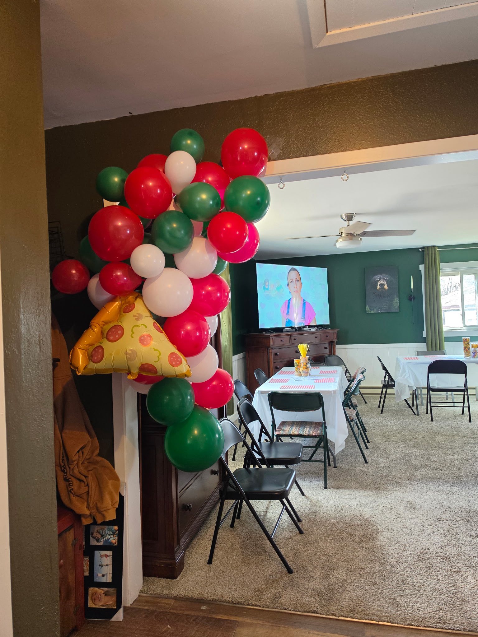 Red, white, and green balloon arch with a pizza-shaped balloon in a living room party setting.