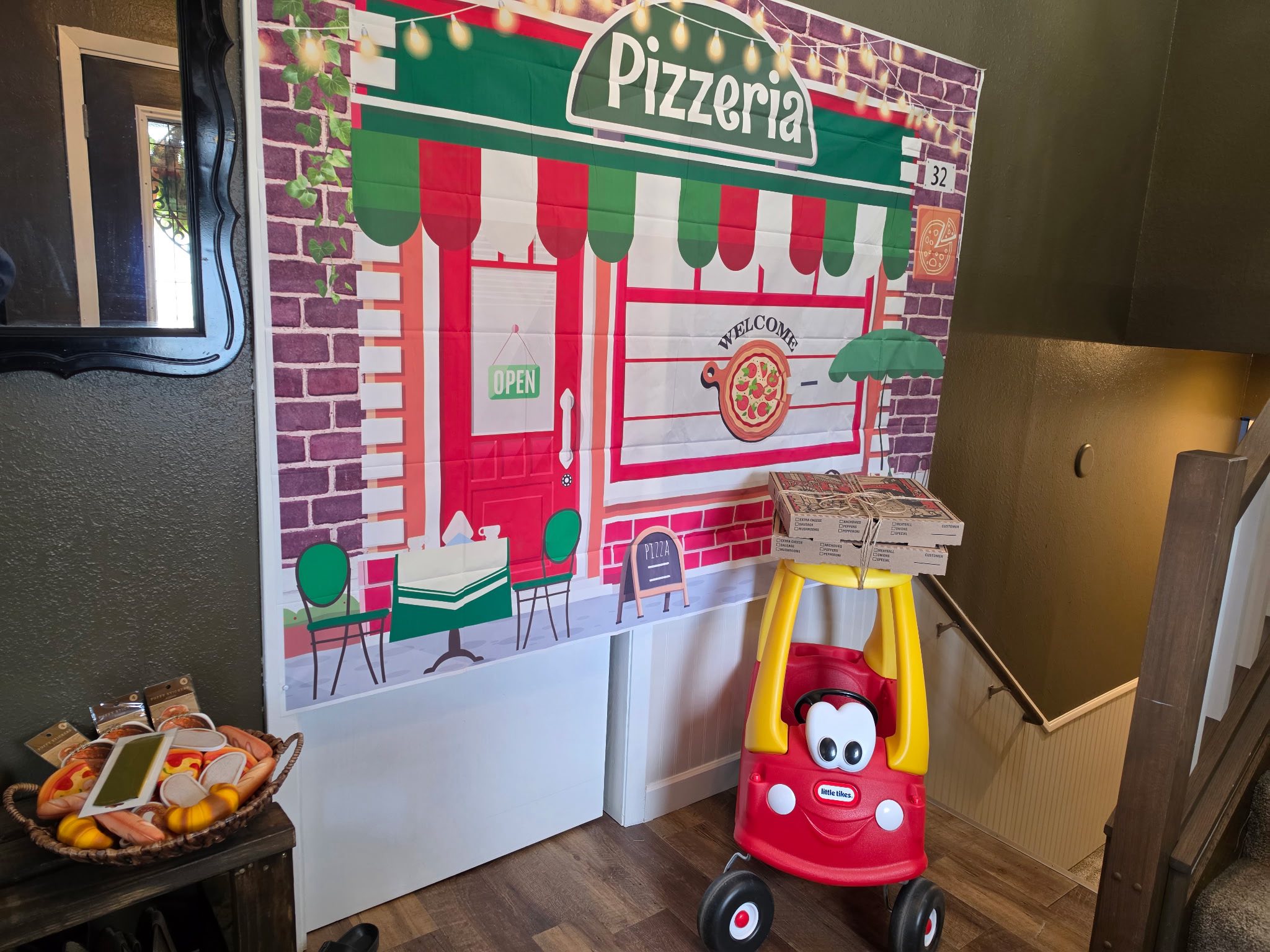 Little Tikes toy car acting as a pizza delivery vehicle in front of a pizzeria-themed party backdrop.