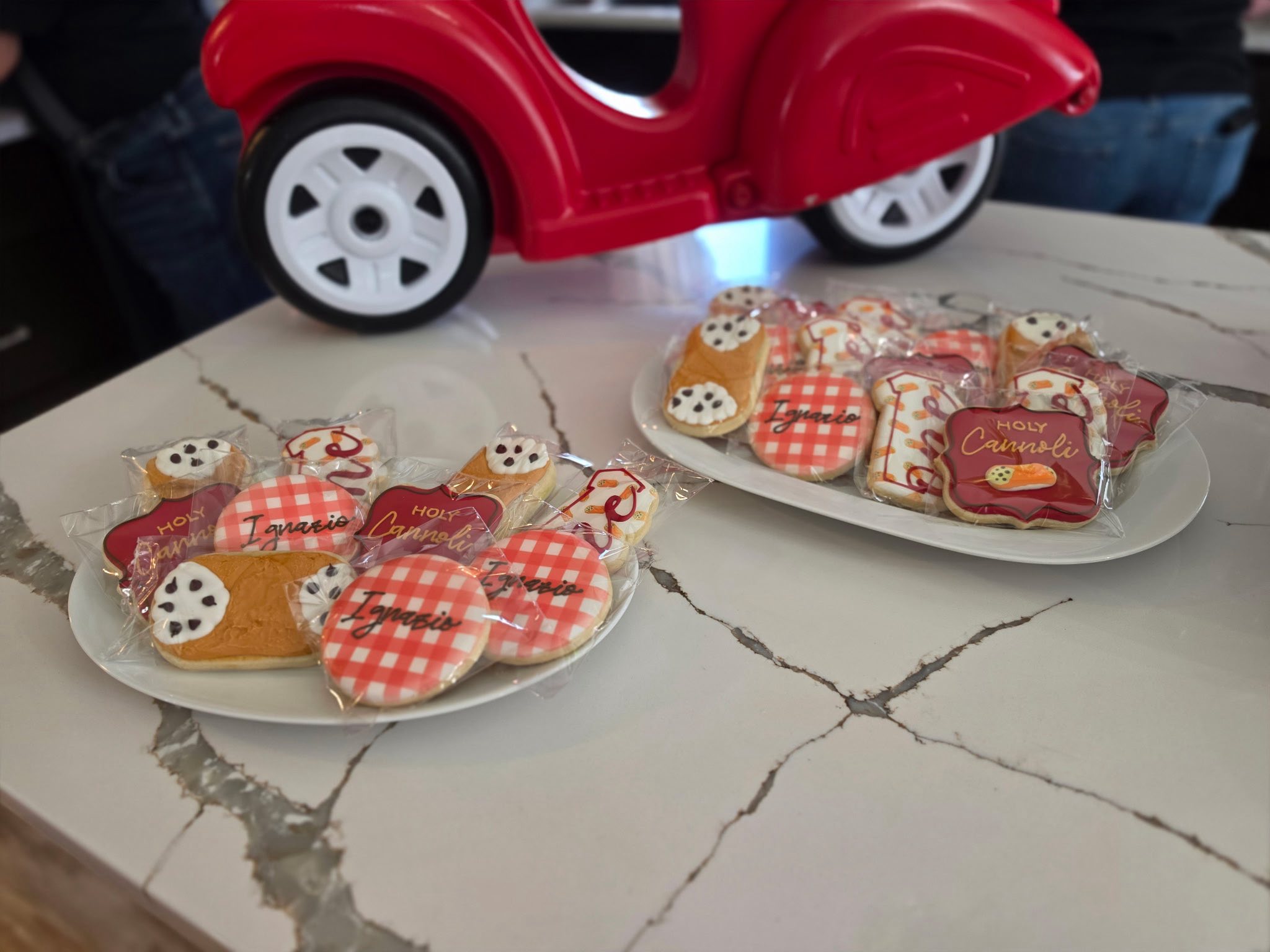 Platters of custom decorated cookies themed as cannolis and red gingham checks for an event.