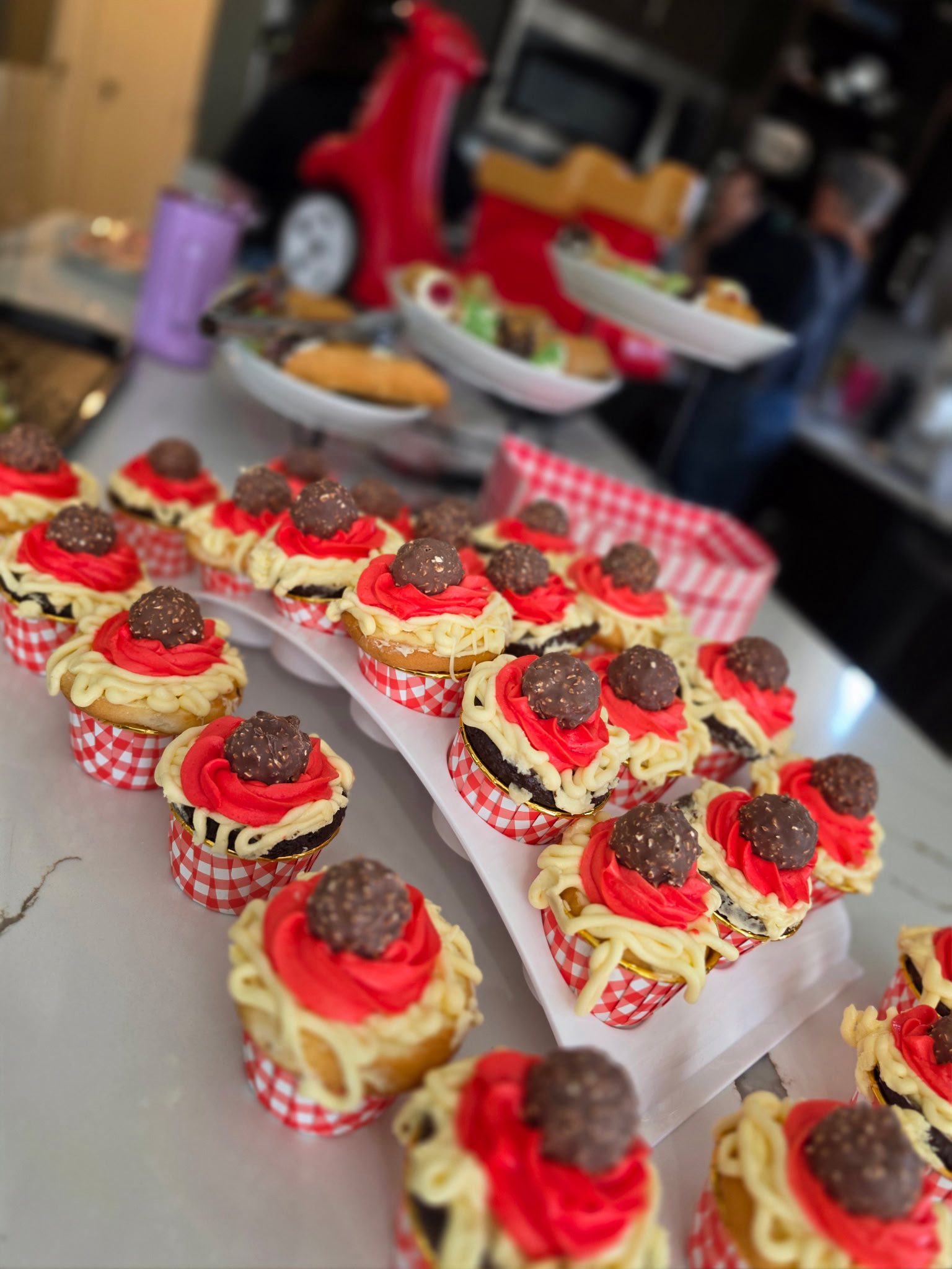 Cupcakes decorated to look like spaghetti with red frosting sauce and a chocolate hazelnut meatball on top.