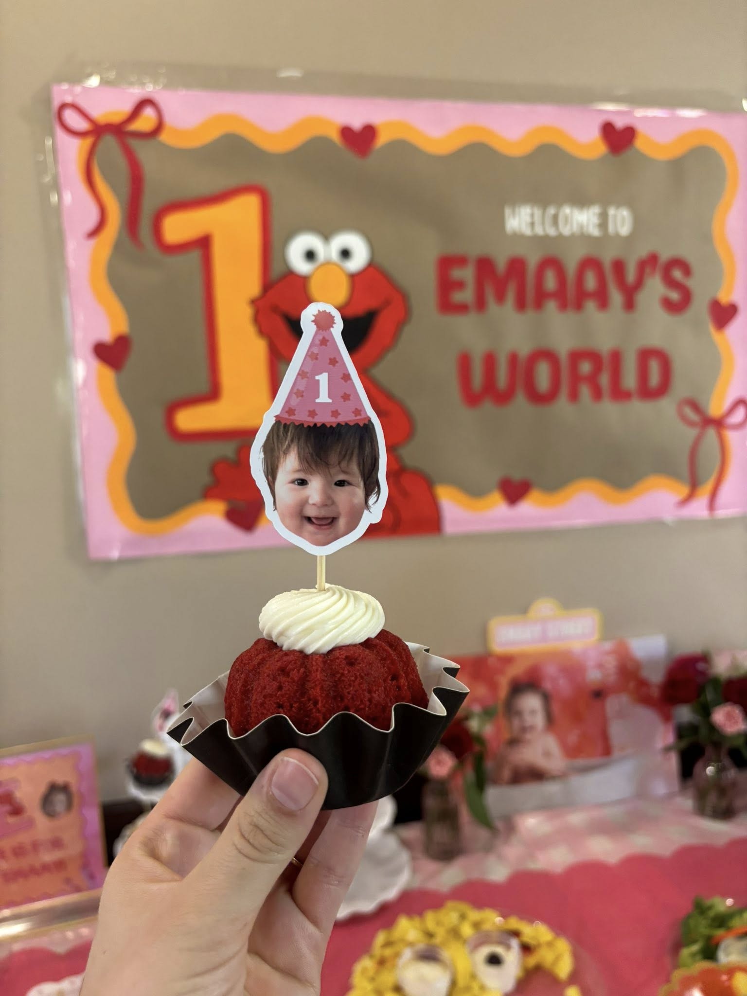Hand holding a mini red velvet cupcake topped with a personalized photo cake topper of a baby wearing a party hat