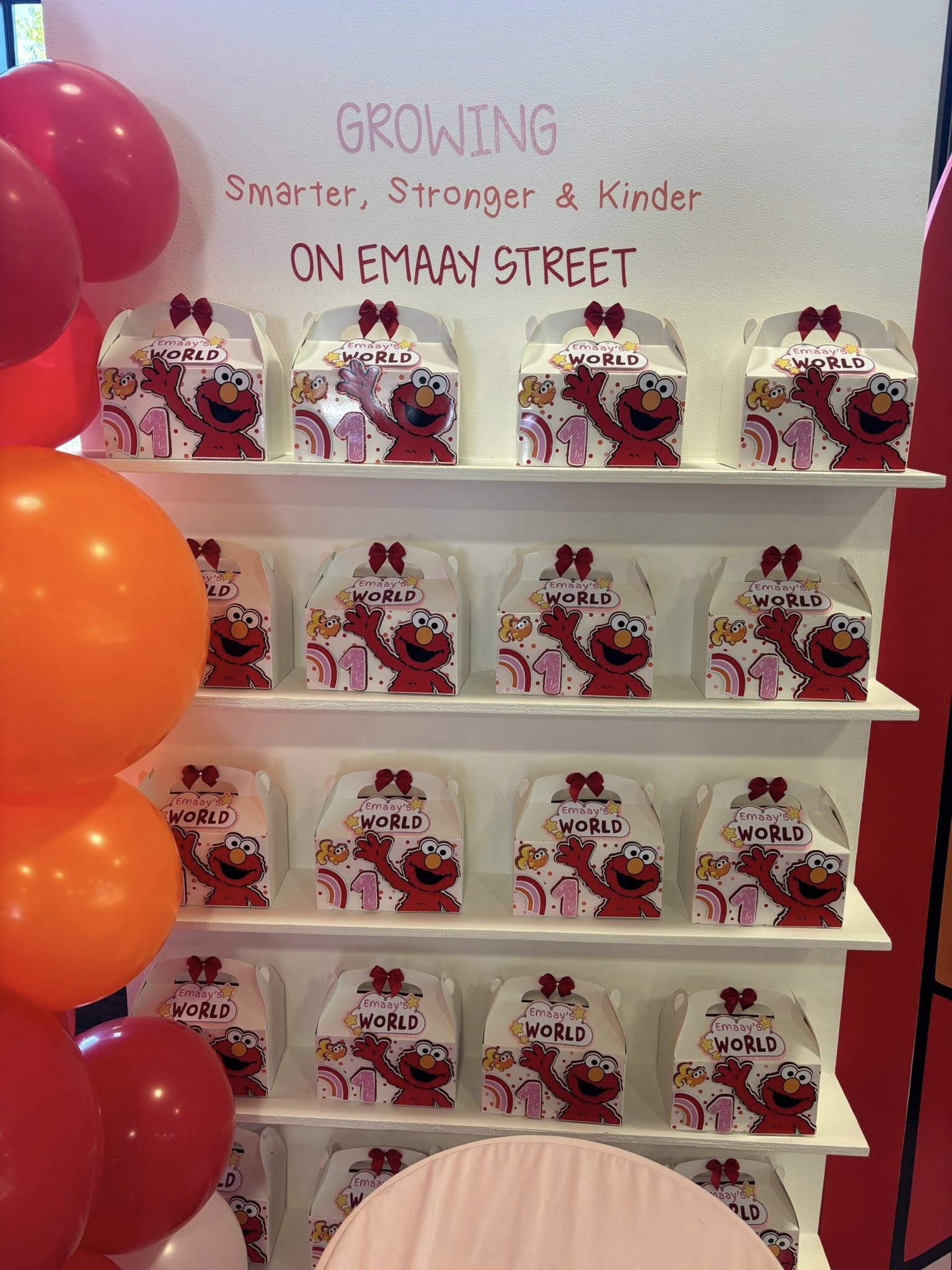 Shelves filled with Elmo themed party favor gift boxes decorated with red bows for a first birthday celebration.