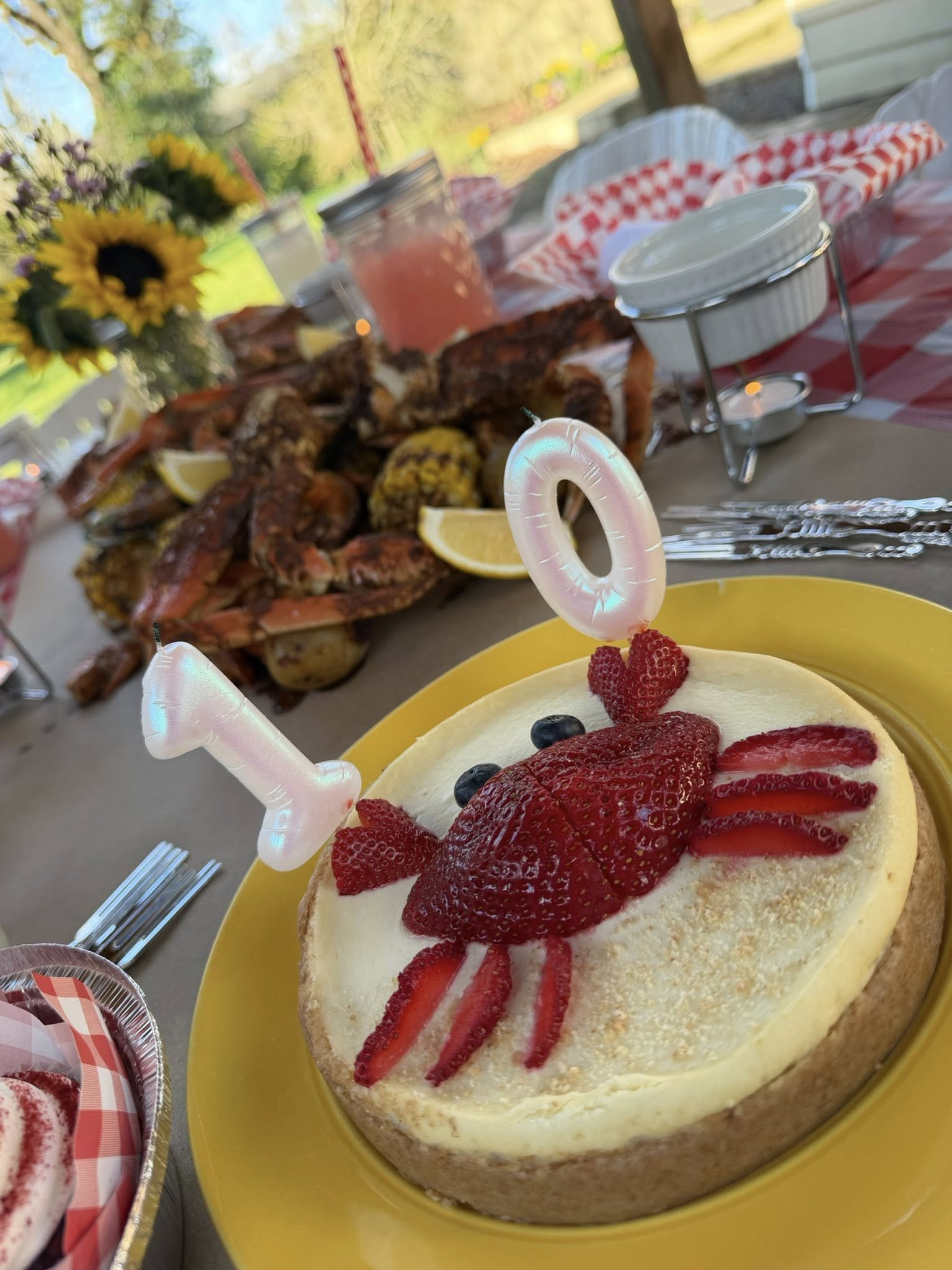 Cheesecake decorated with a strawberry crab and number '10' candles on a table with a crab boil feast.