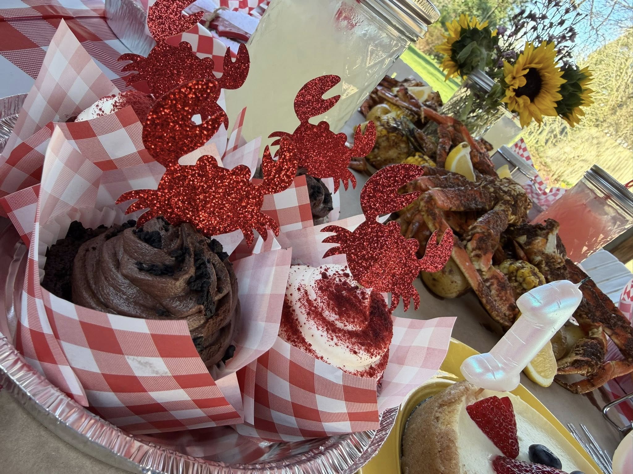 Cupcakes decorated with glittery red crab toppers in red and white checkered wrappers at a crab boil party.
