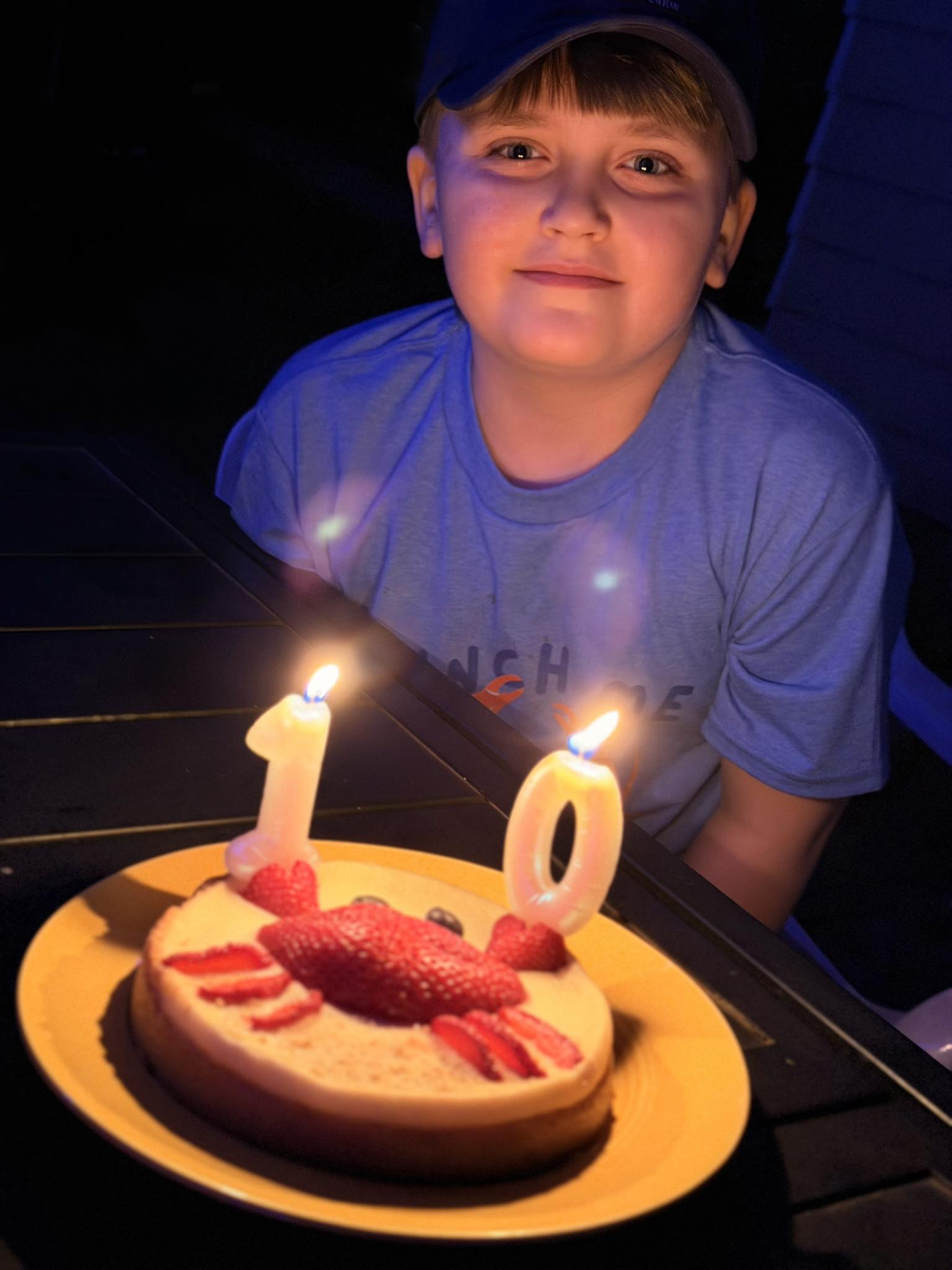 Young boy sitting behind a birthday cake decorated with strawberry crab and number ten candles.