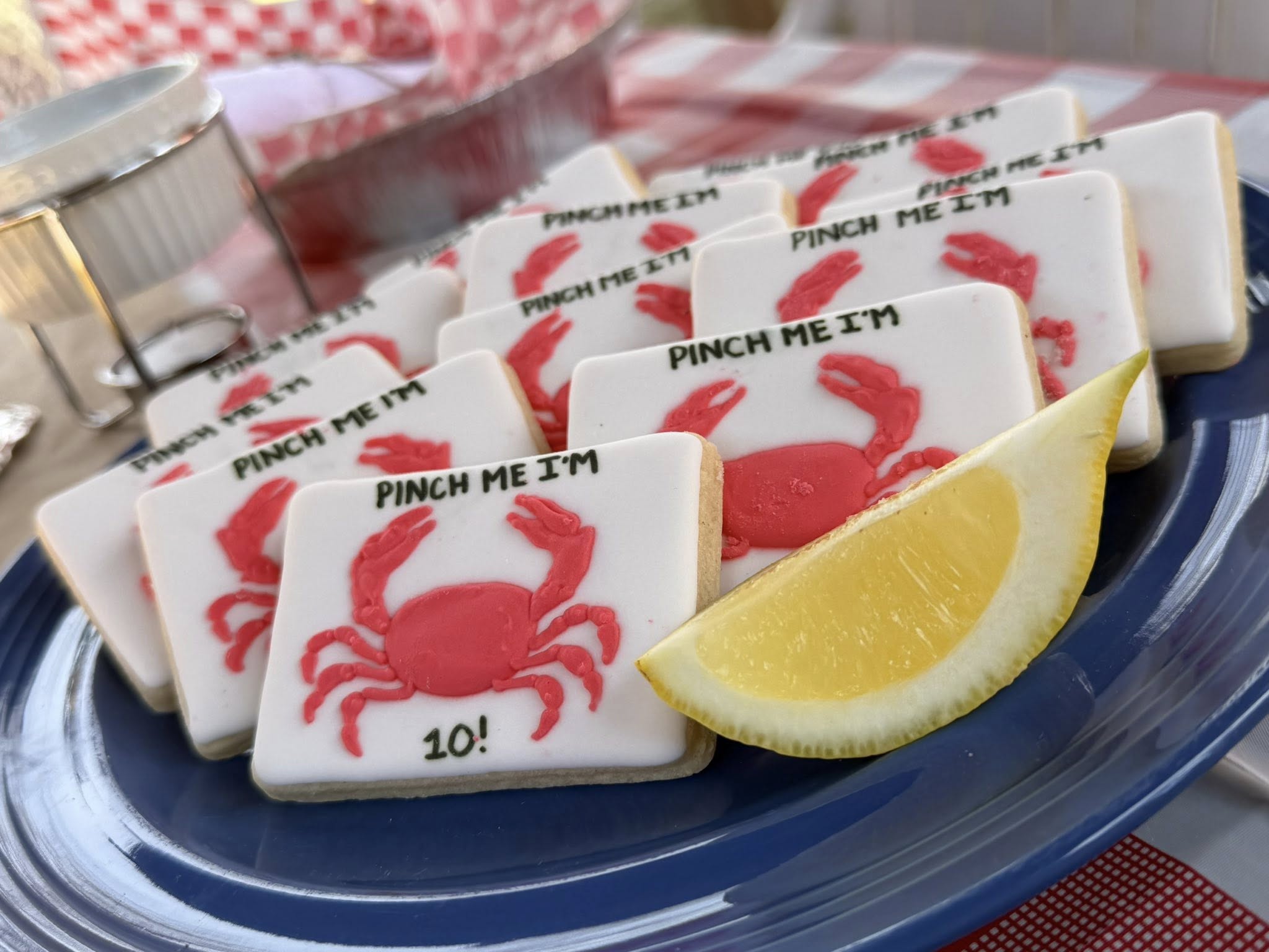 Rectangular sugar cookies decorated with red icing crabs and the text Pinch Me I'm 10 on a blue plate with lemon.