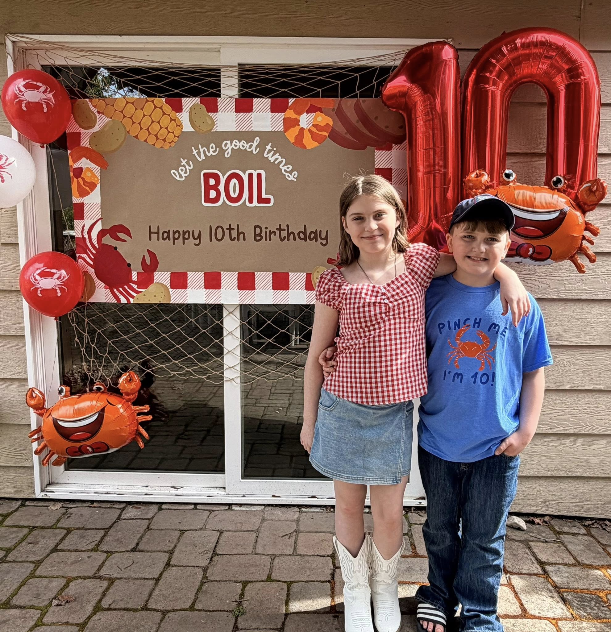 Two smiling children standing in front of a 10th birthday crab boil themed party decoration.