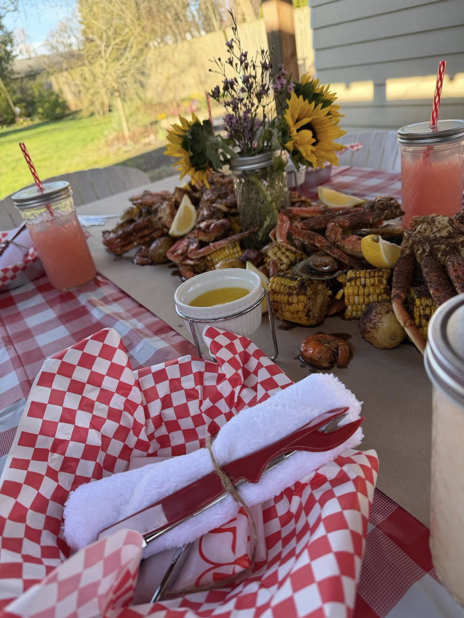 Seafood boil feast with crab legs, corn, and potatoes laid out on a table with a red checkered tablecloth.