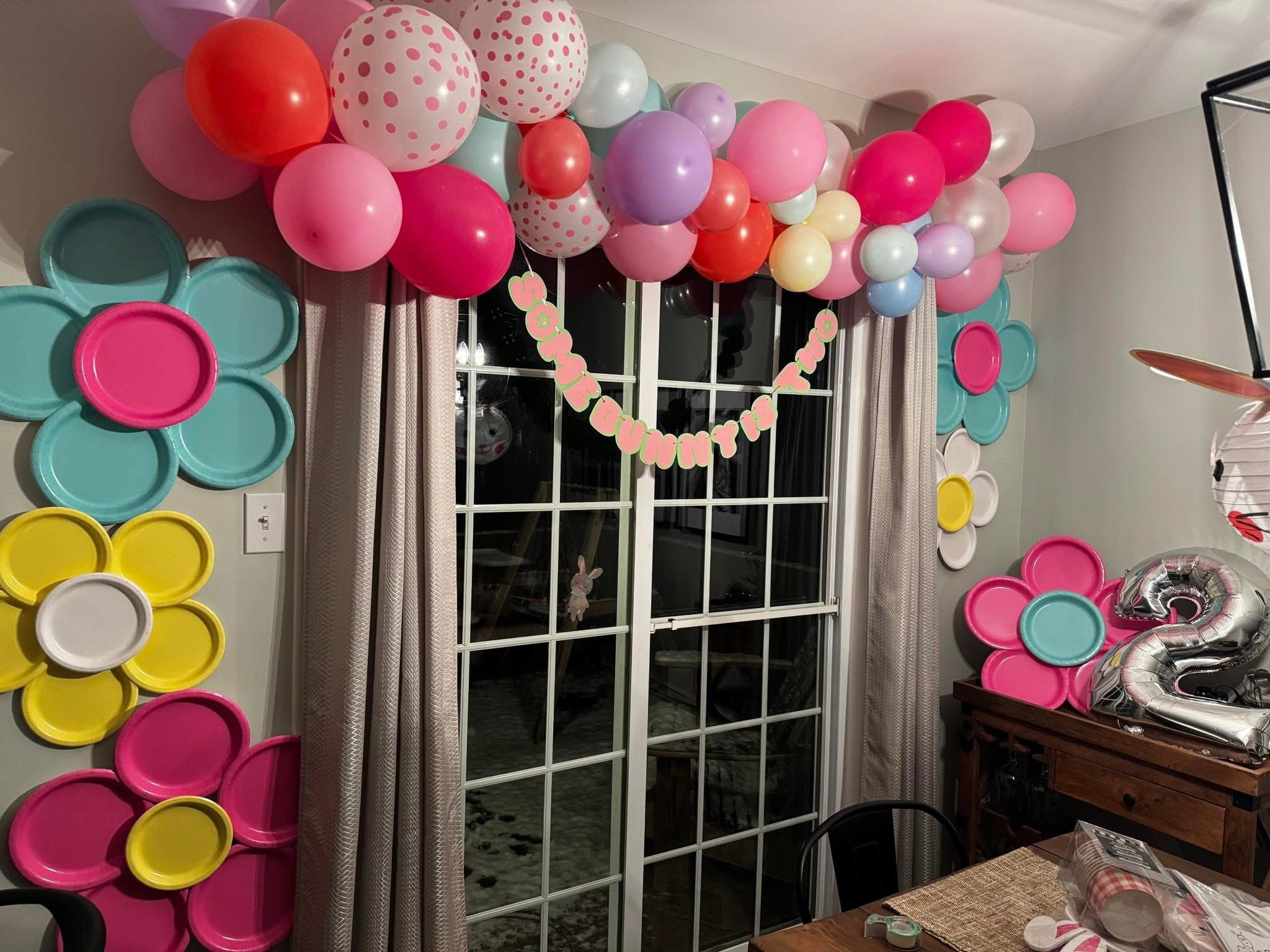 Easter-themed birthday decorations featuring a balloon arch, paper plate flowers, and a Some Bunny is Two banner.