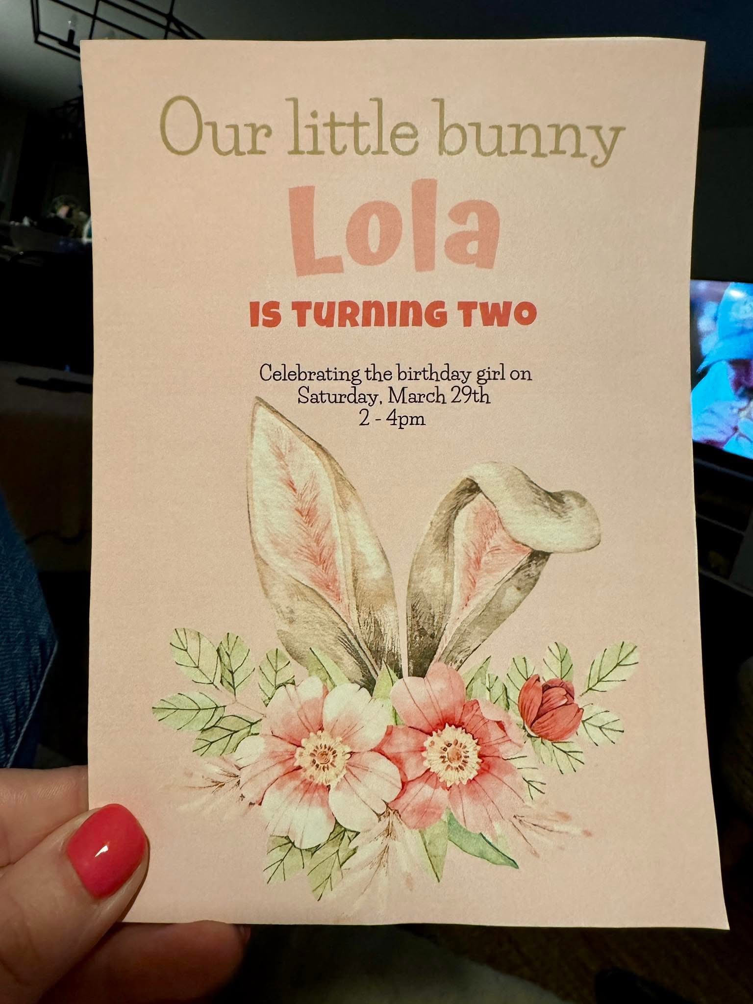 Invitation for Lola's second birthday featuring bunny ears and watercolor flowers on a blush background.