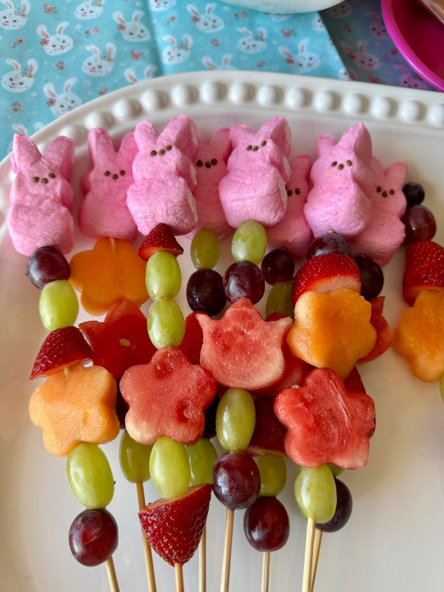 Fruit skewers featuring star-shaped melon, grapes, strawberries, and pink marshmallow bunnies on a platter.