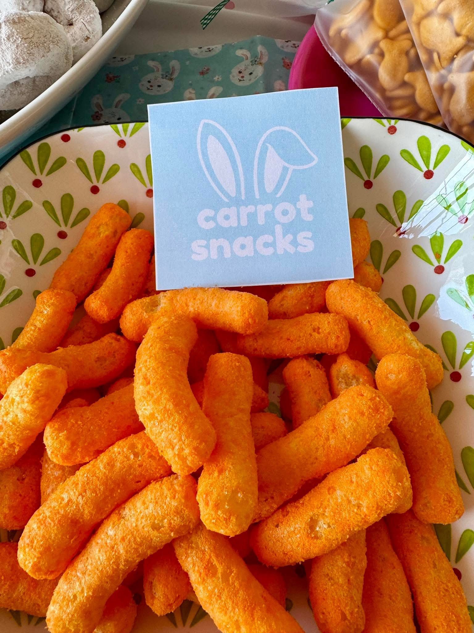Bowl of orange cheese puffs with a sign that says carrot snacks and has bunny ears.