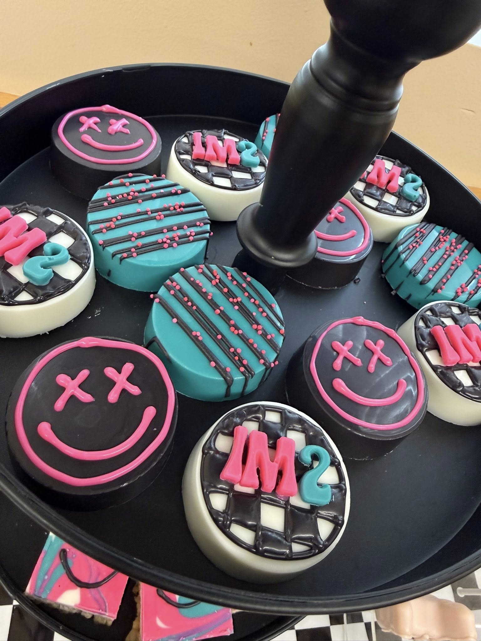 Assorted decorated chocolate sandwich cookies for a second birthday party on a black stand.