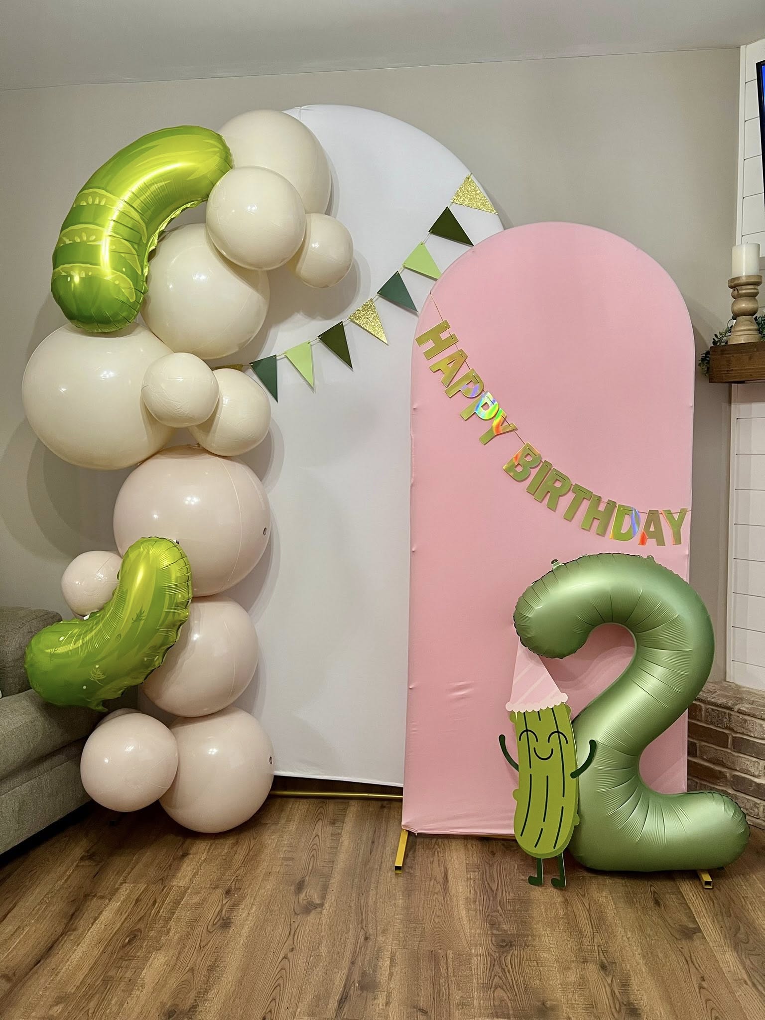 Pickle themed second birthday party backdrop with pink and white panels, balloon arch, and number 2 balloon.