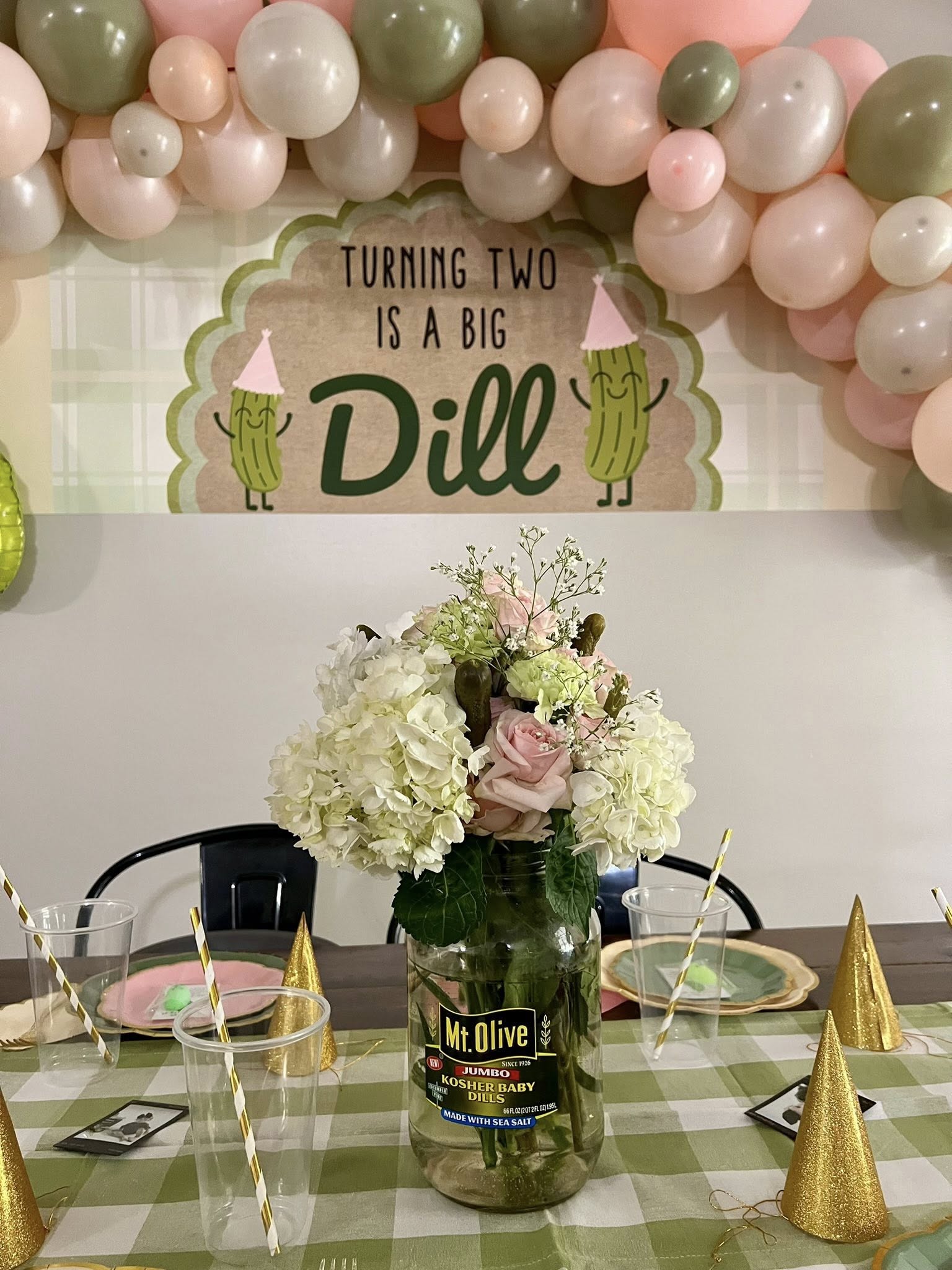 Birthday table centerpiece made from a Mt. Olive pickle jar filled with white and pink flowers under a sign that reads Turning Two Is A Big Dill