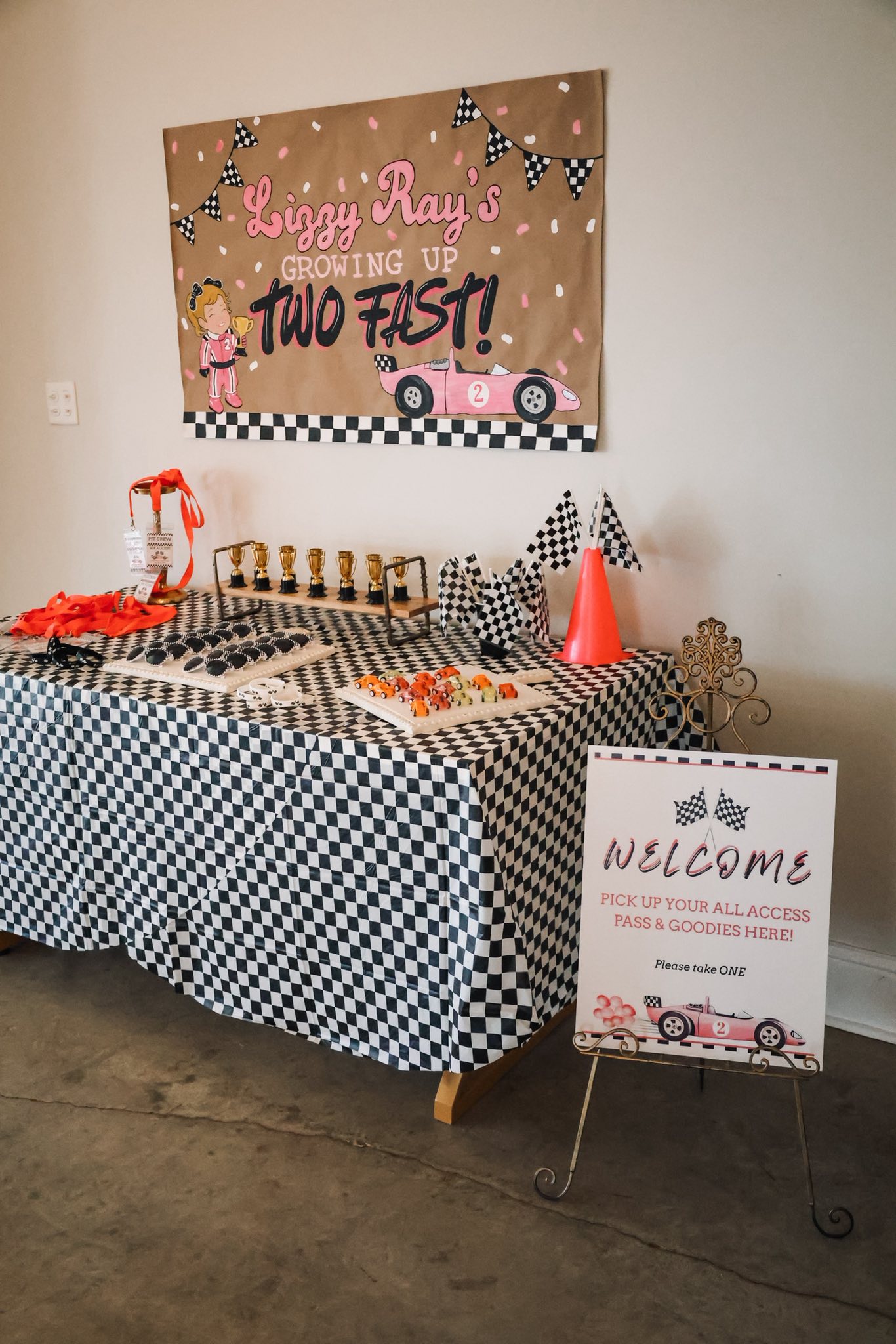 Race car-themed party welcome table with checkered cloth, party favors, and themed signs.
