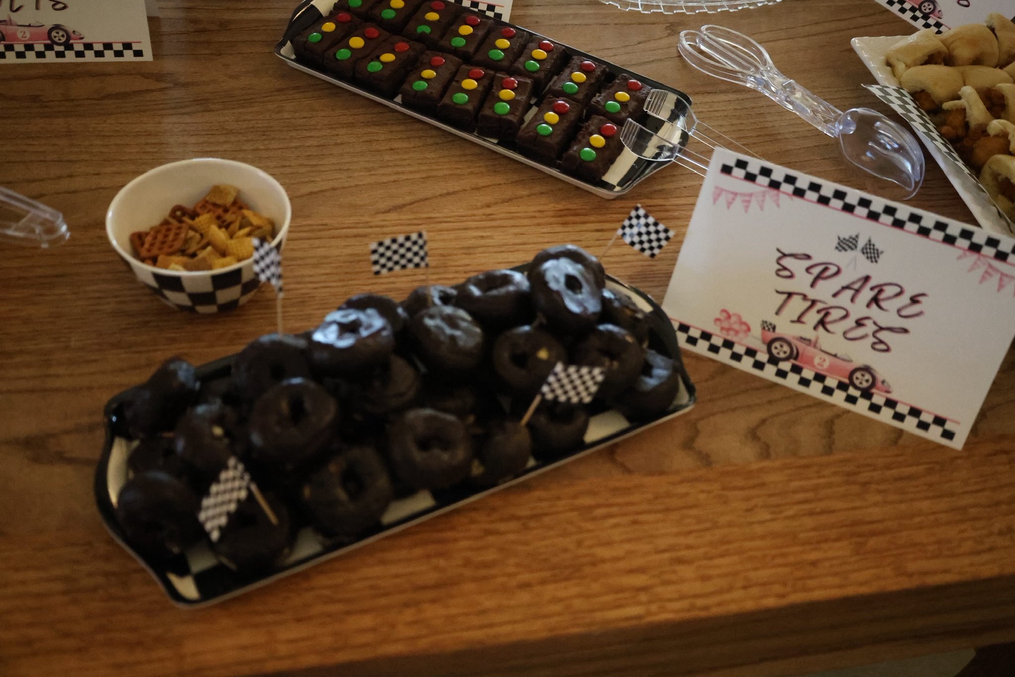 Platter of chocolate doughnuts labeled Spare Tires with race car themed decor on a dessert table.