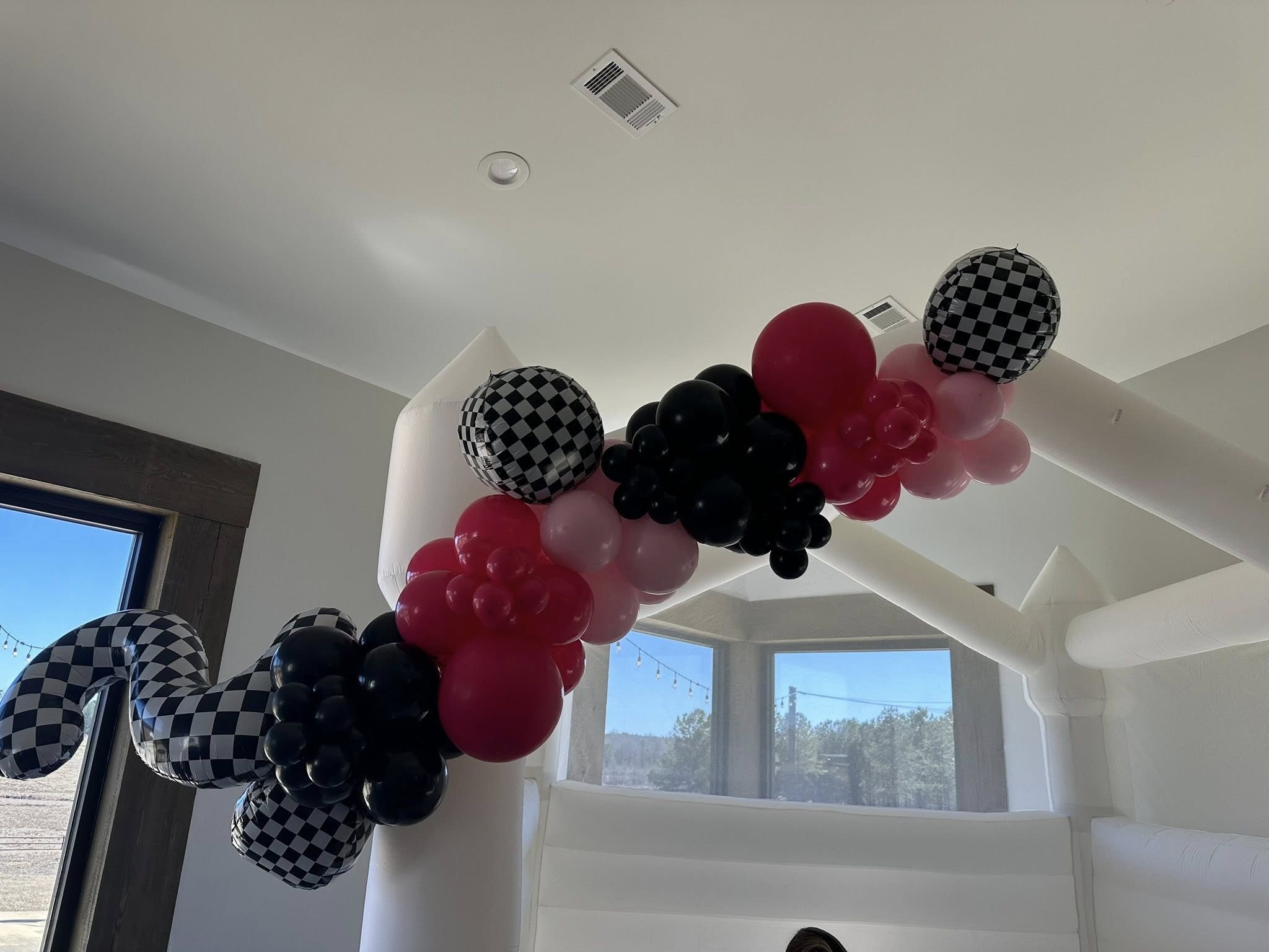 Racing-themed balloon garland with pink, black, and checkered balloons for a bounce house