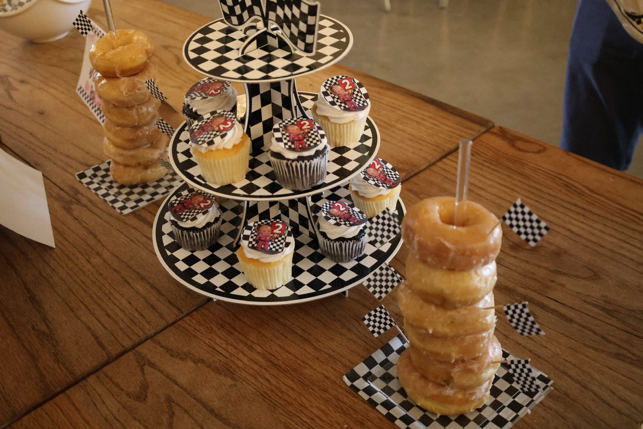 Three-tiered cupcake stand with racing-themed decor and donut stacks on a wooden table.