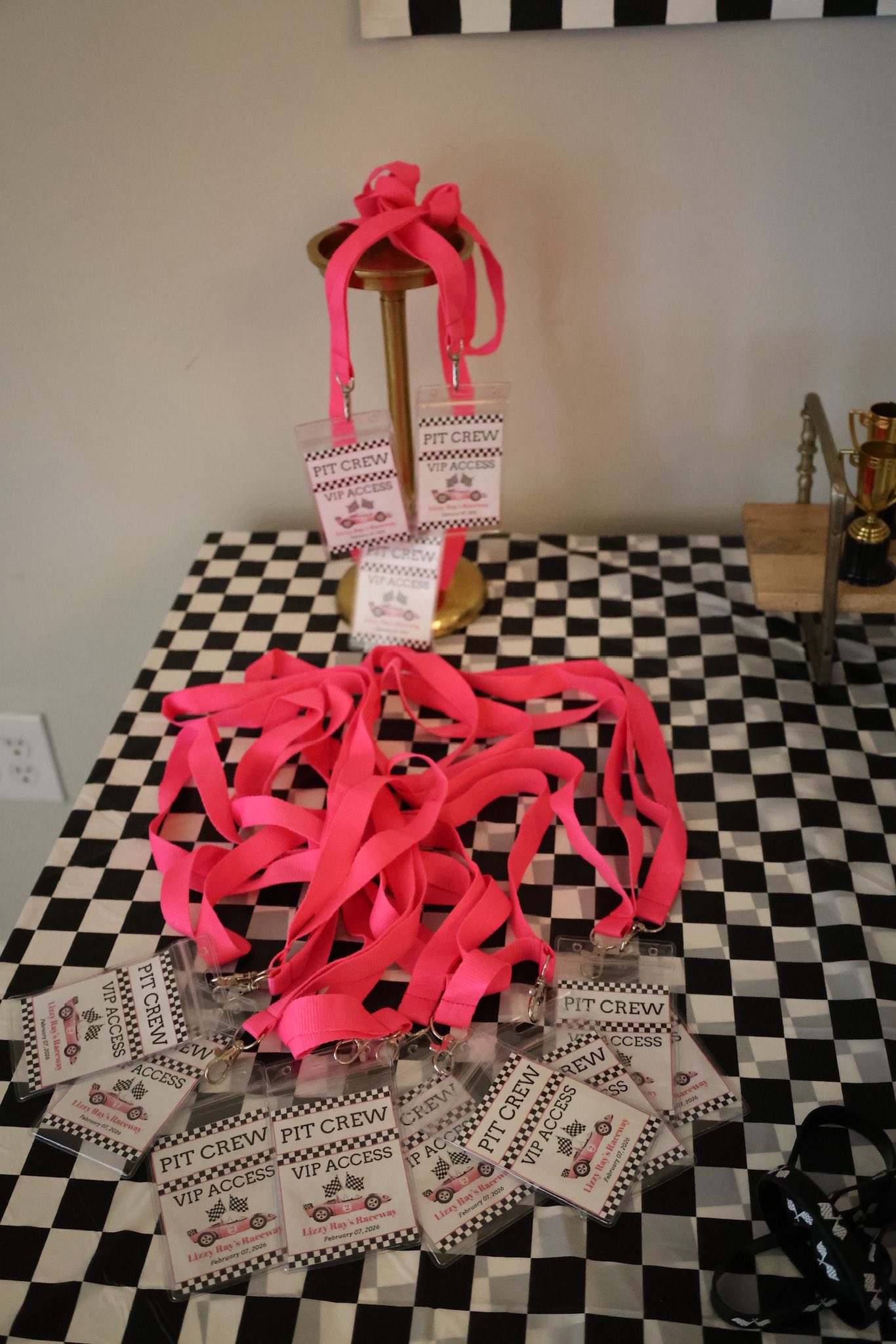 Stack of pink Pit Crew VIP access lanyards and laminated race-themed badges on a checkered tablecloth.