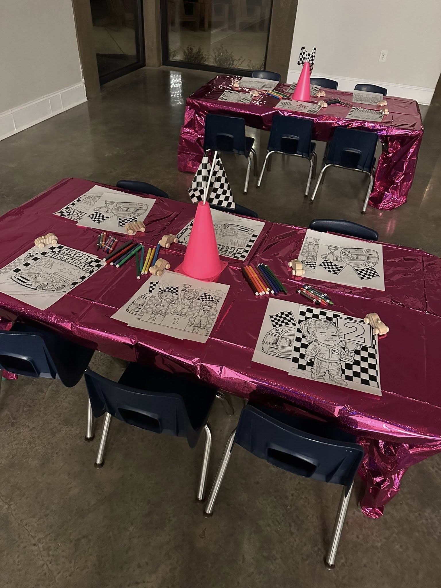 Tables set for a race car themed birthday party with coloring sheets, toy cars, and checkered flag props.