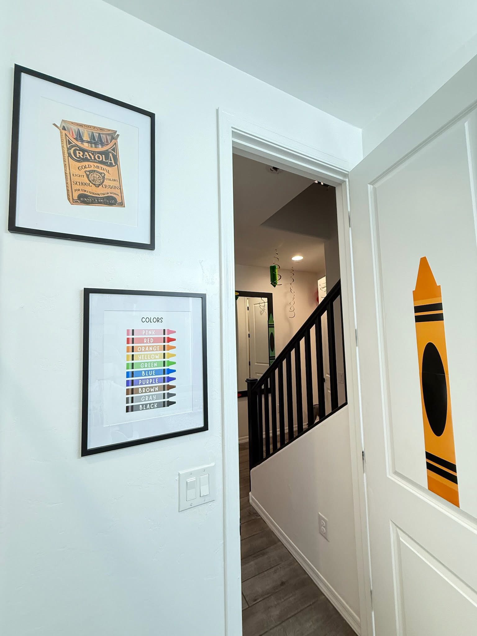 Two framed crayon-themed prints hanging on a white wall next to a door with a large yellow crayon sticker.