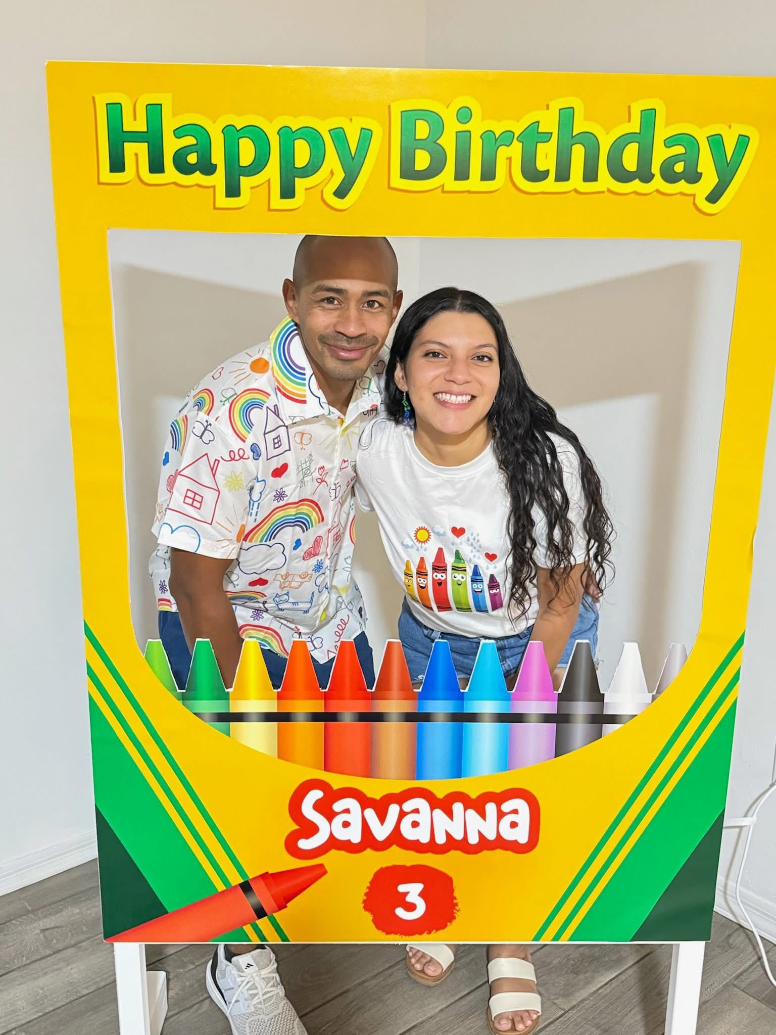 Couple posing behind a custom yellow crayon-themed birthday photo frame for Savanna's 3rd birthday.
