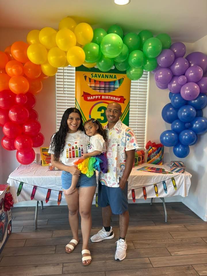 Family celebrating a third birthday with a crayon-themed backdrop and balloon arch