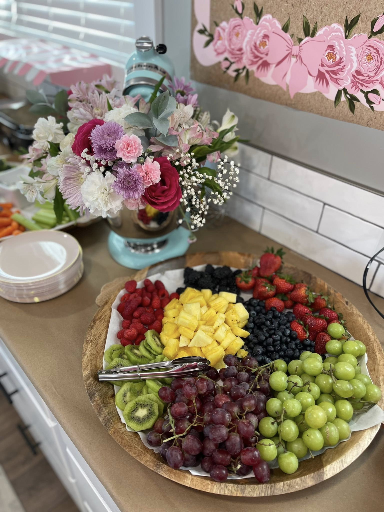 Large wooden platter filled with fresh assorted fruit including pineapple, grapes, berries, and kiwi slices.