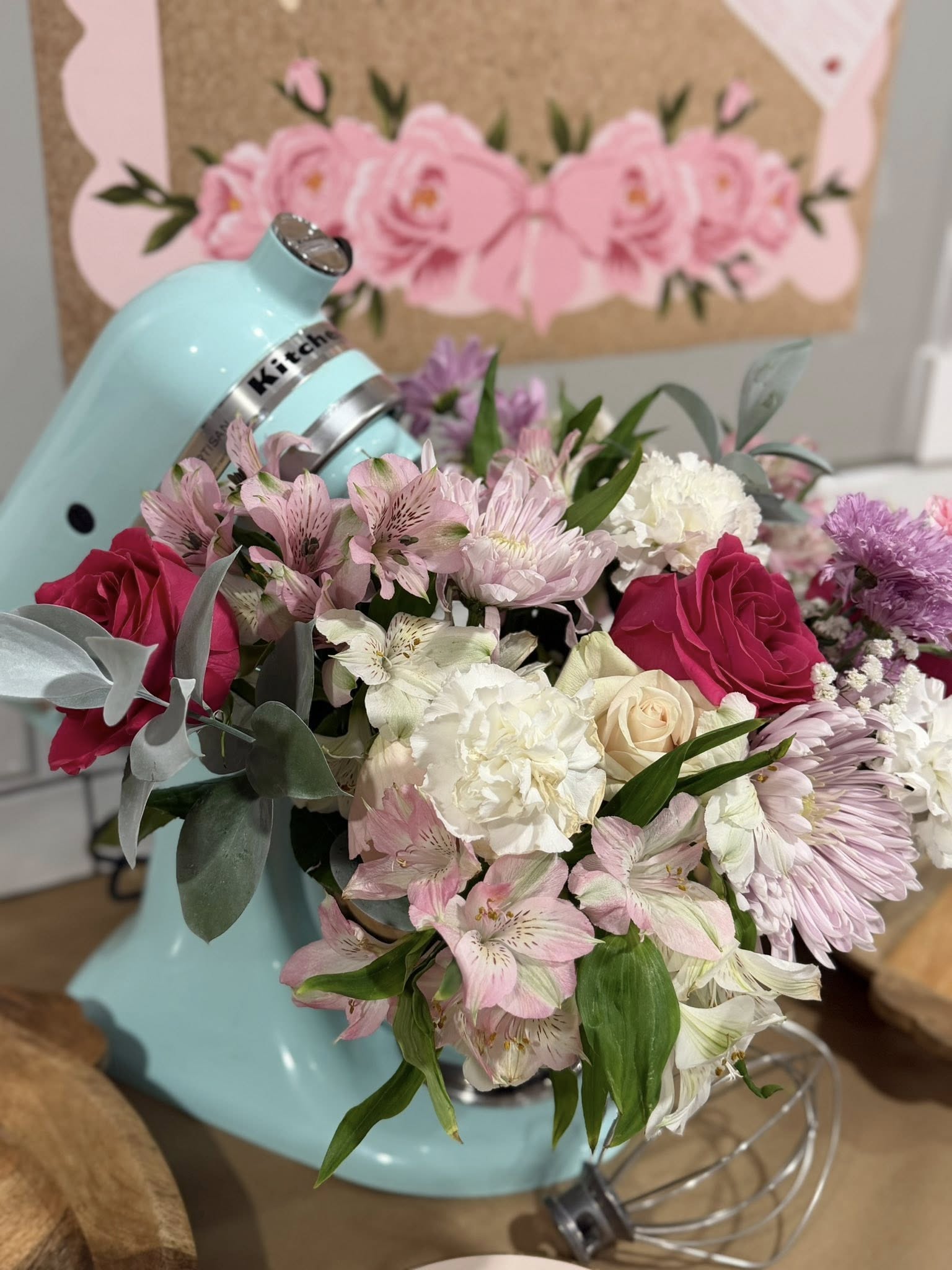 Light blue stand mixer filled with a vibrant bouquet of pink roses, white carnations, and alstroemeria flowers.