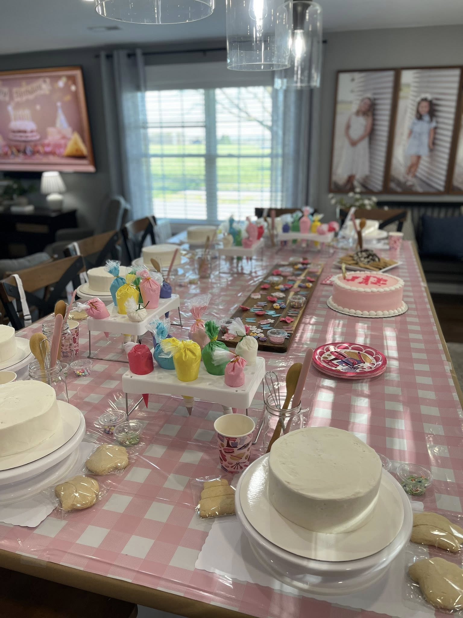 Dining table set up for a cake decorating party with blank cakes, icing bags, and assorted sprinkles.
