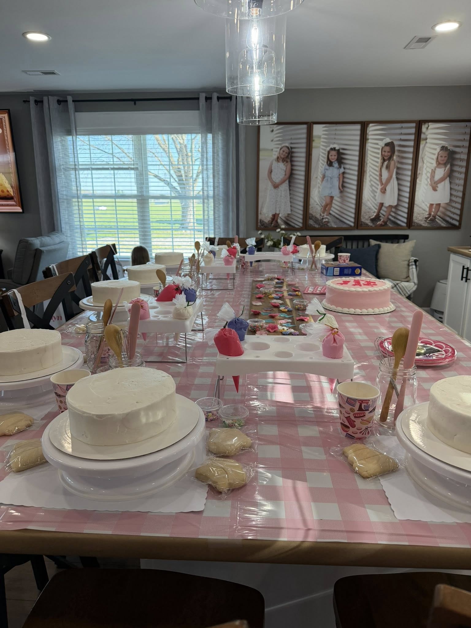 Dining table set up for a cake decorating party featuring multiple plain cakes, piping bags, and cookies.