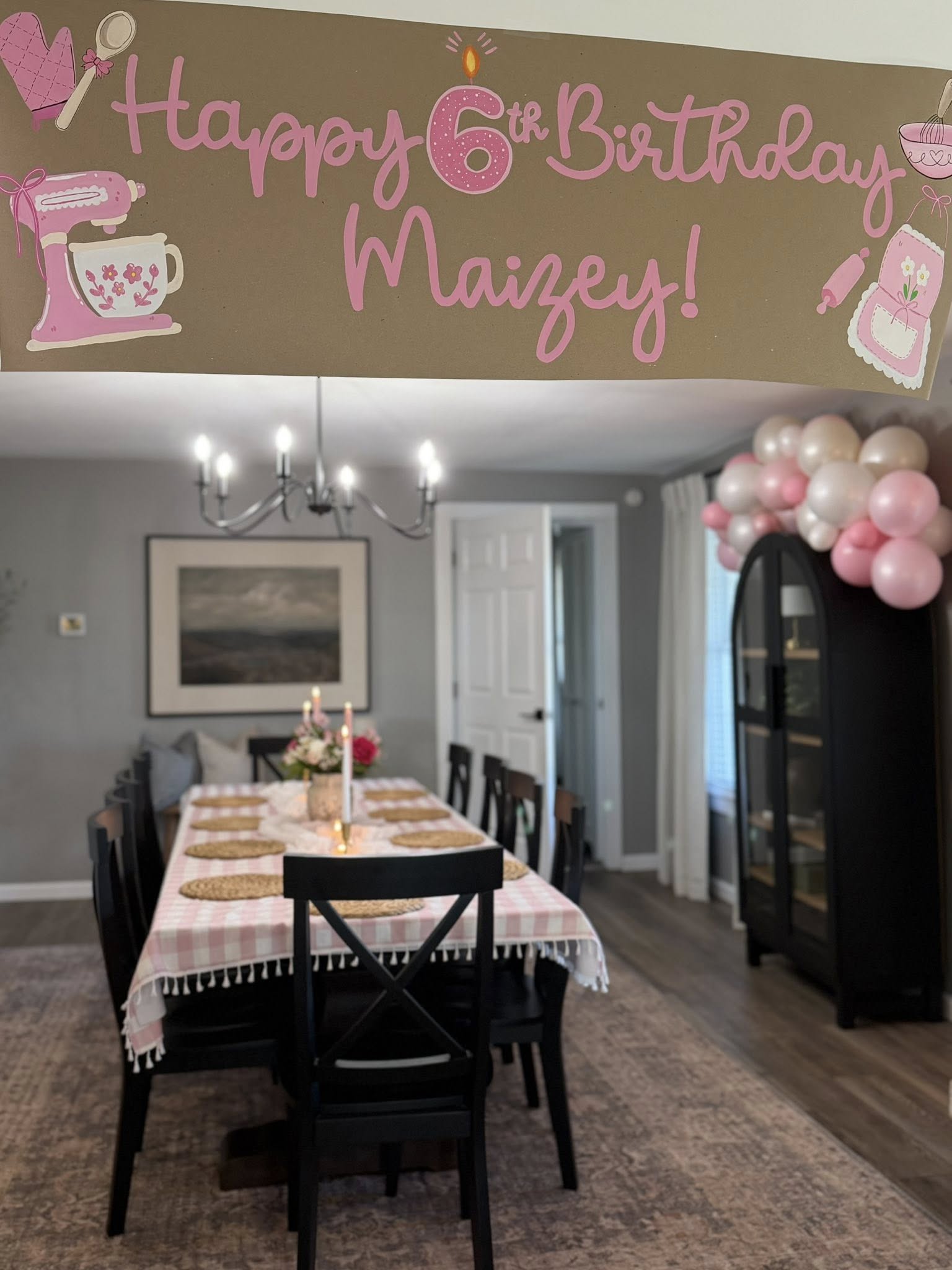 Dining room decorated for a 6th birthday with a pink baking-themed banner hanging in the foreground.