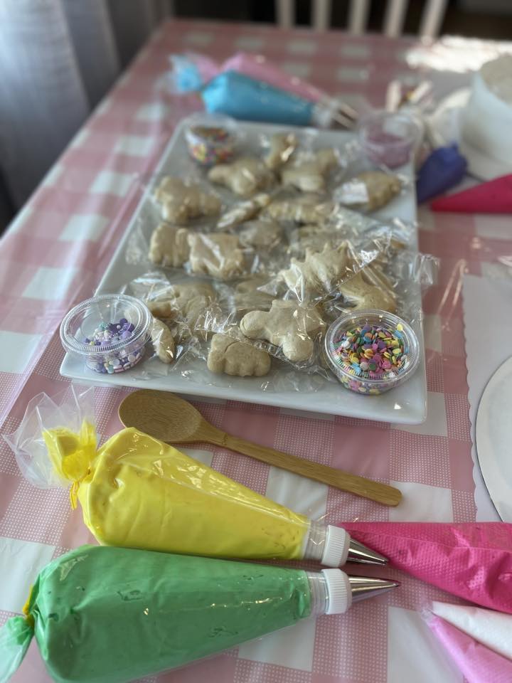 Platter of wrapped sugar cookies with containers of colorful sprinkles and icing piping bags for decorating