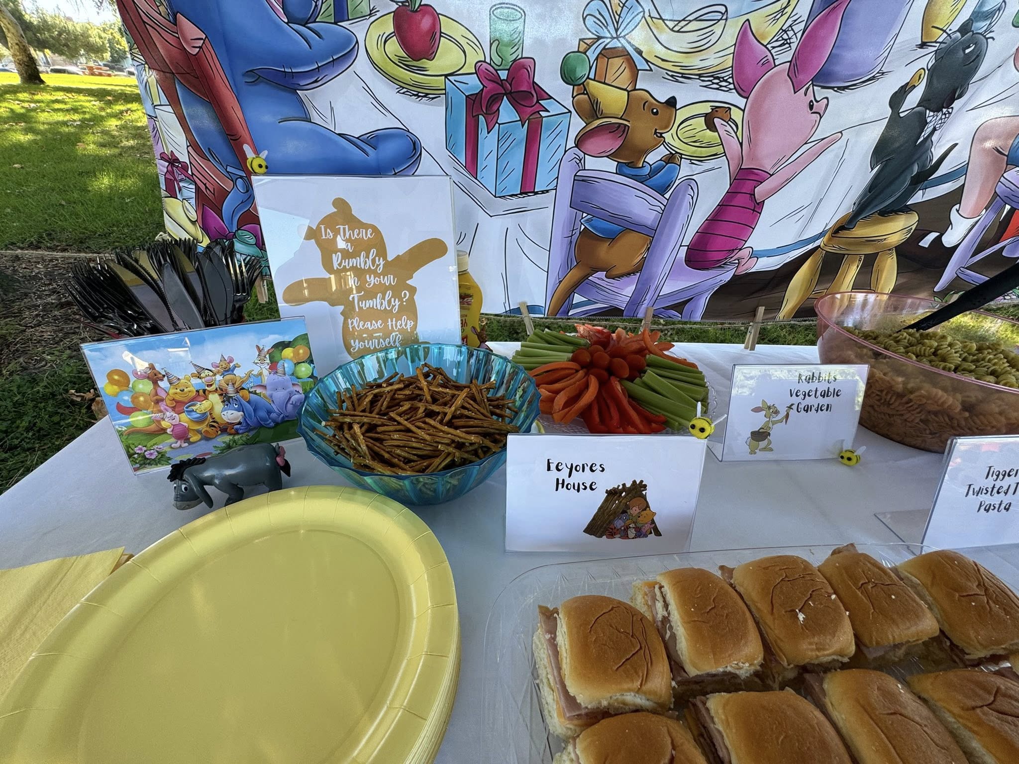 Winnie the Pooh themed party food table with snacks, labeled dishes, and decorations.