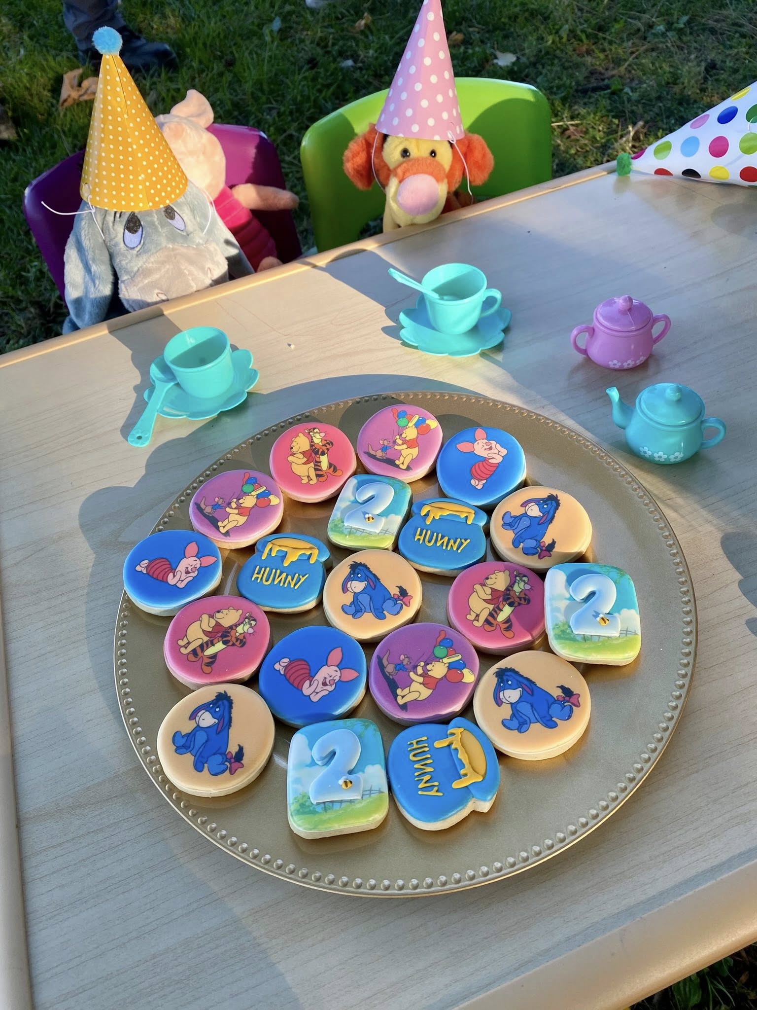 Winnie the Pooh themed birthday cookies for a two year old, arranged on a gold platter with toy tea set accessories.