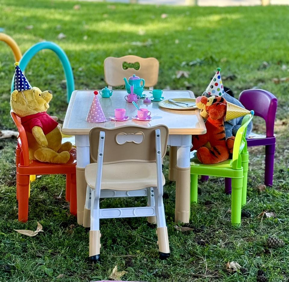 Winnie the Pooh and Tigger plush toys wearing party hats at a colorful plastic children's table setting outdoors.