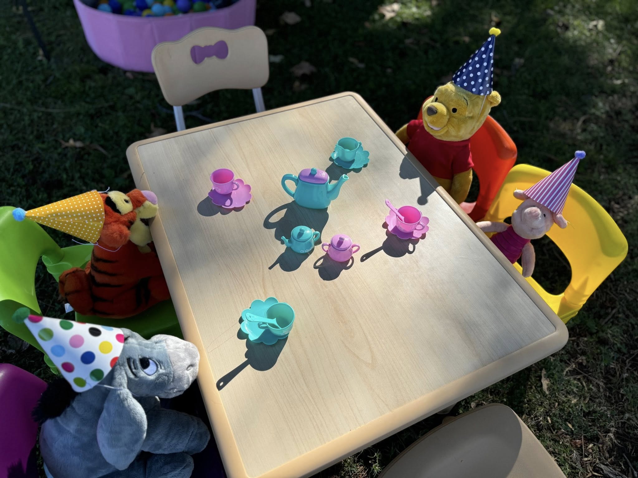 Winnie the Pooh characters wearing party hats around a miniature play tea table set