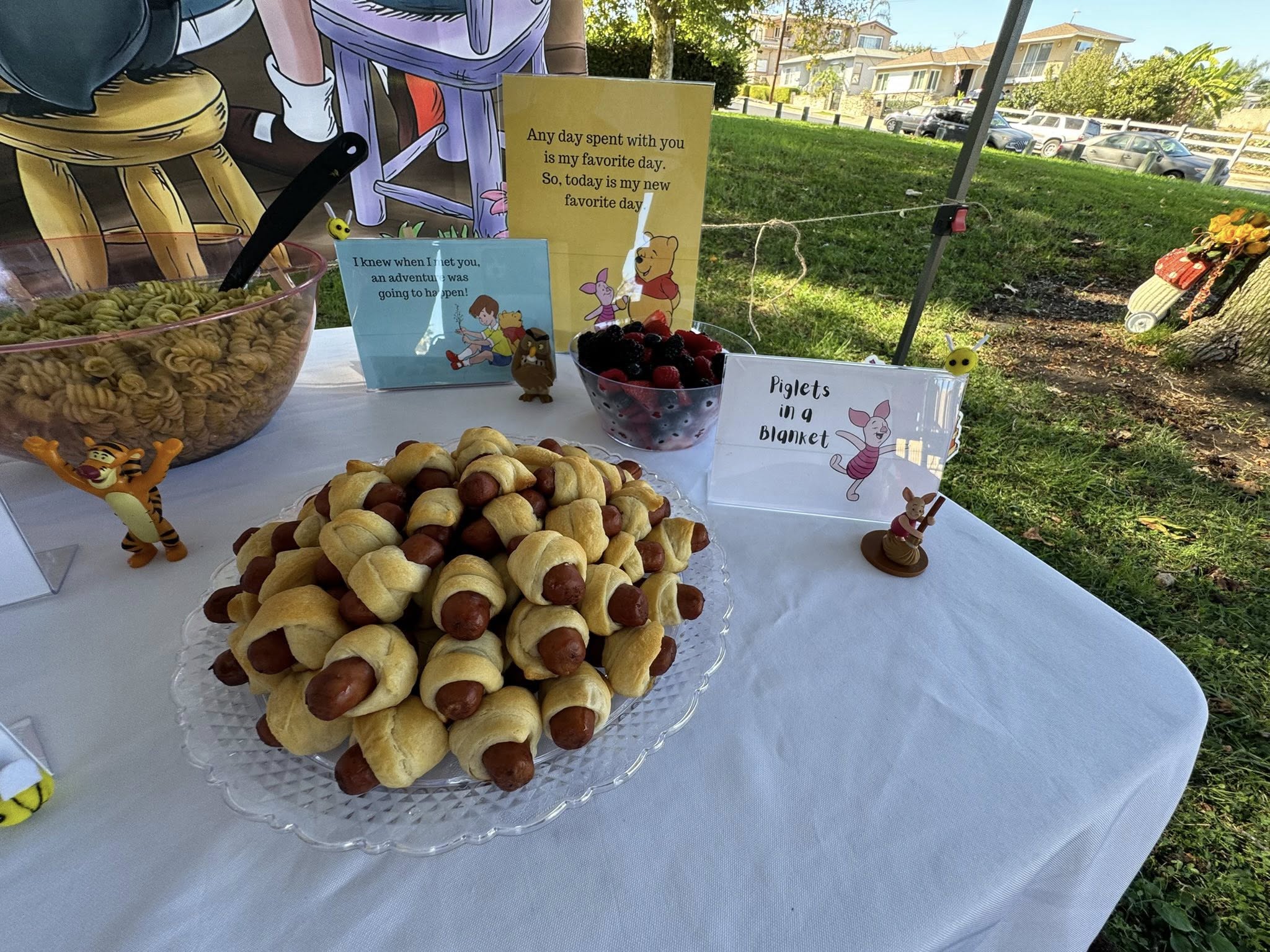 Platter of Piglets in a Blanket appetizer at a Winnie the Pooh themed party with matching character signage.
