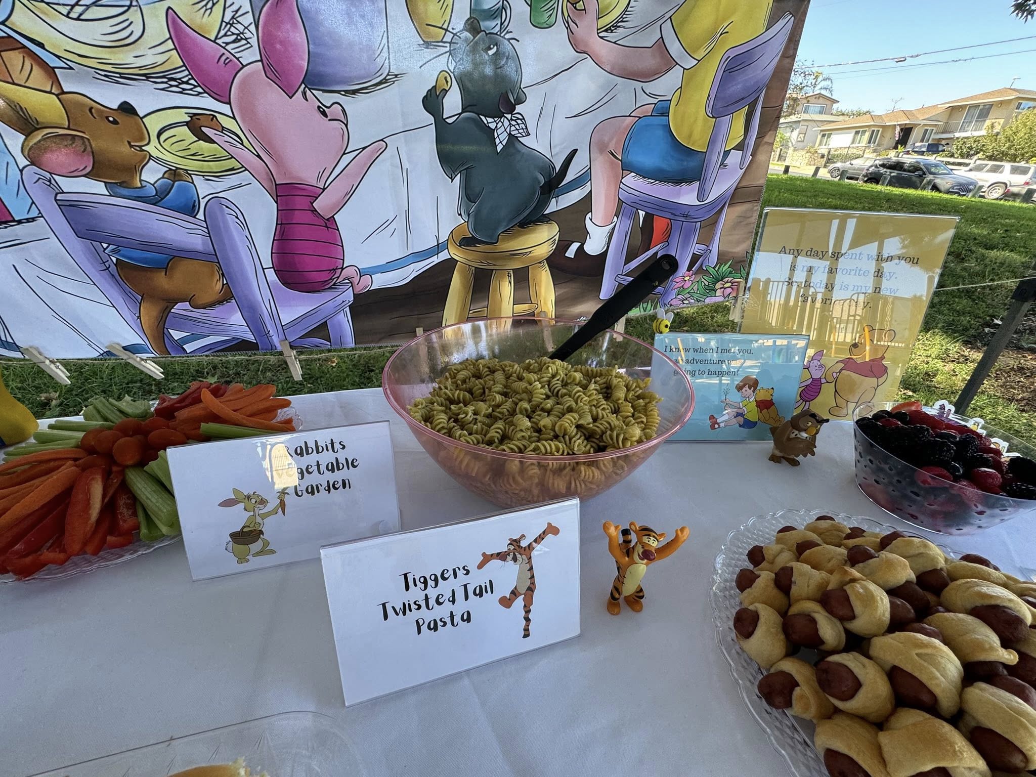 Winnie the Pooh themed party table with pasta, vegetable platter, and pigs in a blanket.