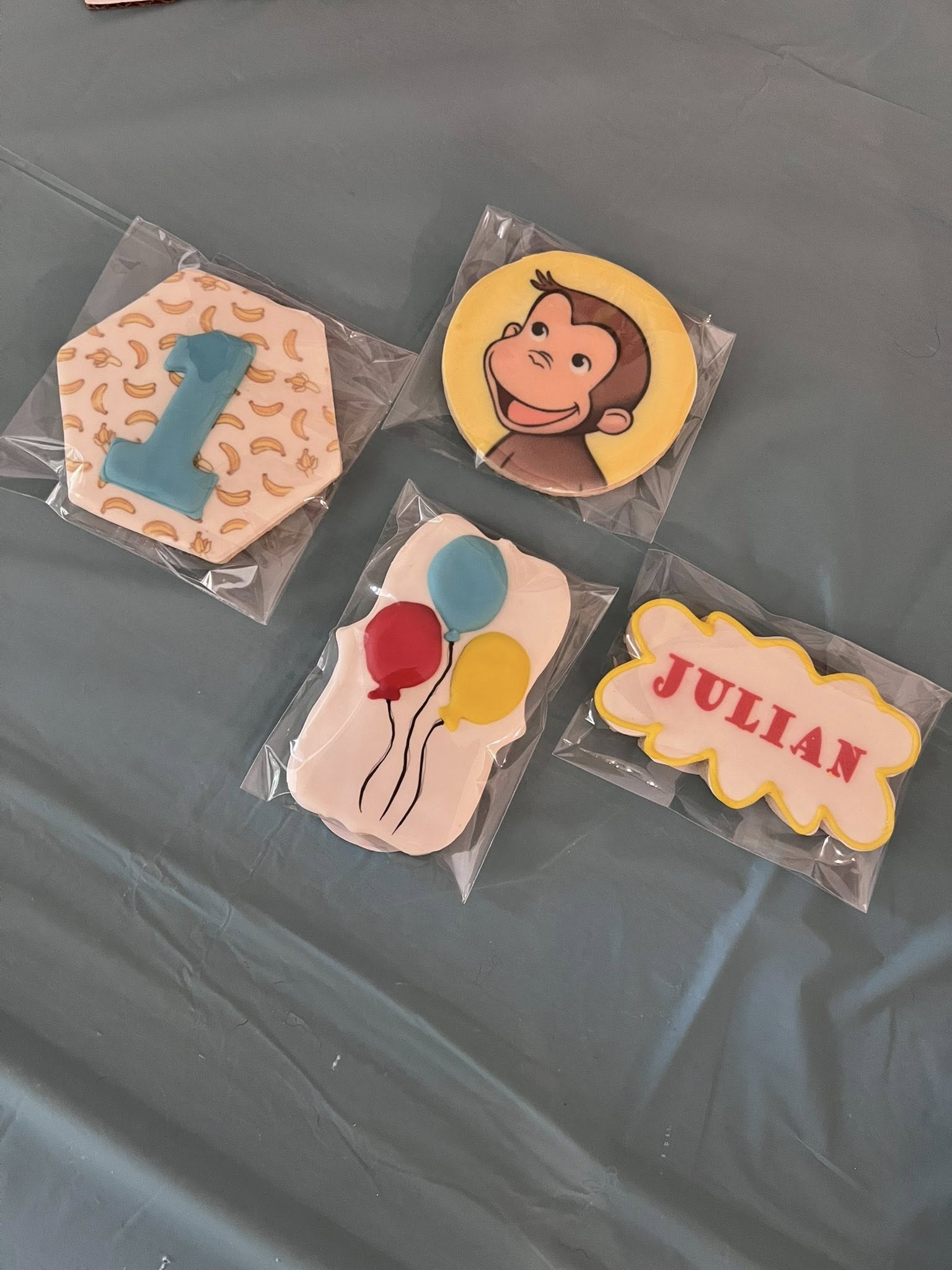 Set of four Curious George themed birthday sugar cookies including a number one, monkey, balloons, and name plaque.