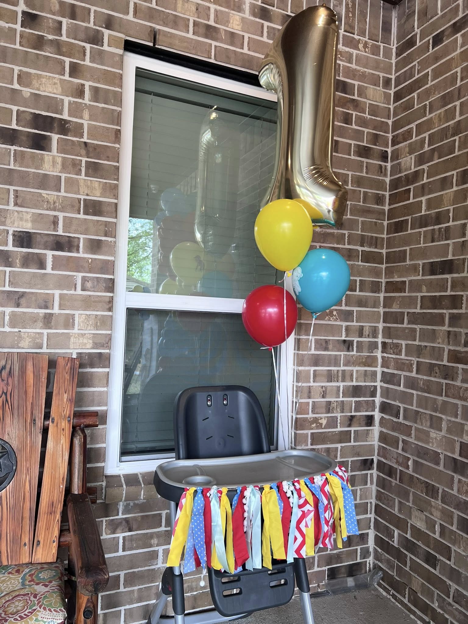 High chair decorated with a colorful fabric garland, featuring a gold number one balloon and small party balloons.