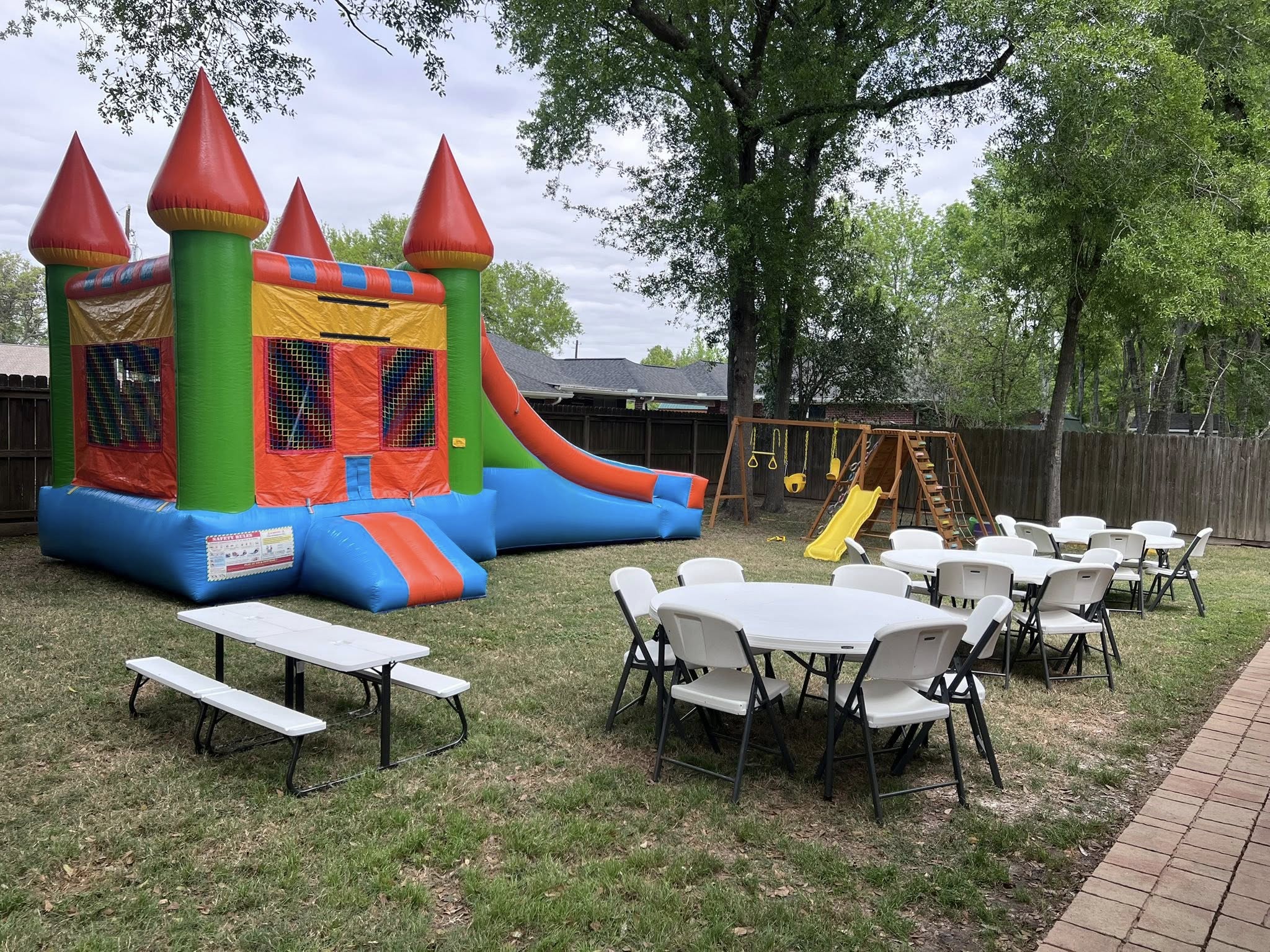 Colorful inflatable bounce house with slide set up in a backyard with party tables and chairs for kids.