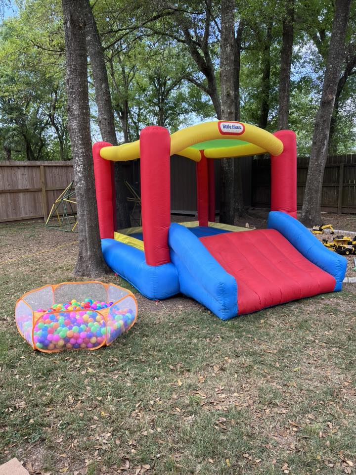 Little Tikes bounce house with slide set up in a backyard next to a ball pit.